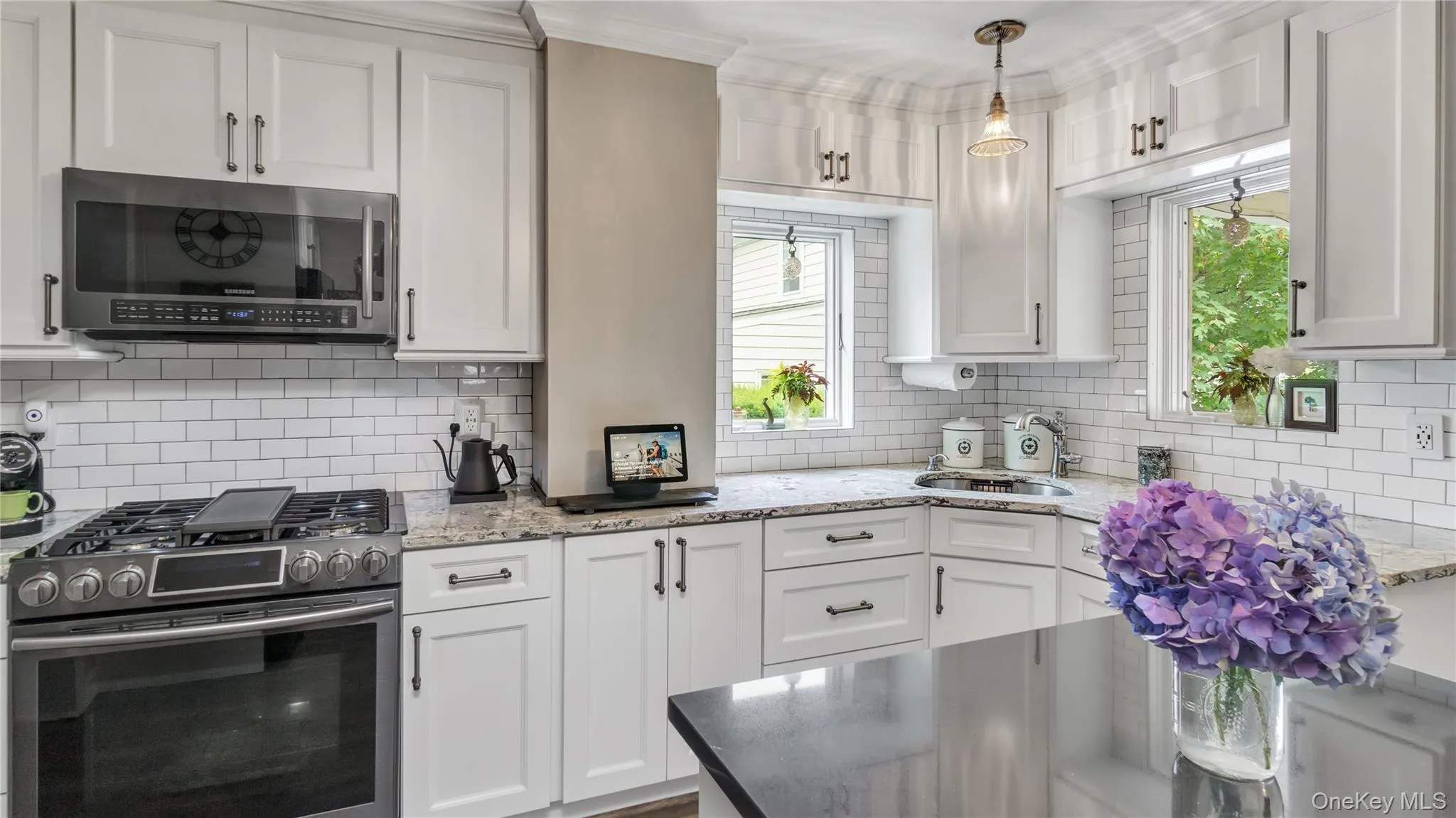 Kitchen with healthy amount of natural light, appliances with stainless steel finishes, light stone counters, white cabinetry, and crown molding Kitchen with healthy amount of natural light, appliances with stainless steel finishes, light stone counters, white cabinetry, and crown molding