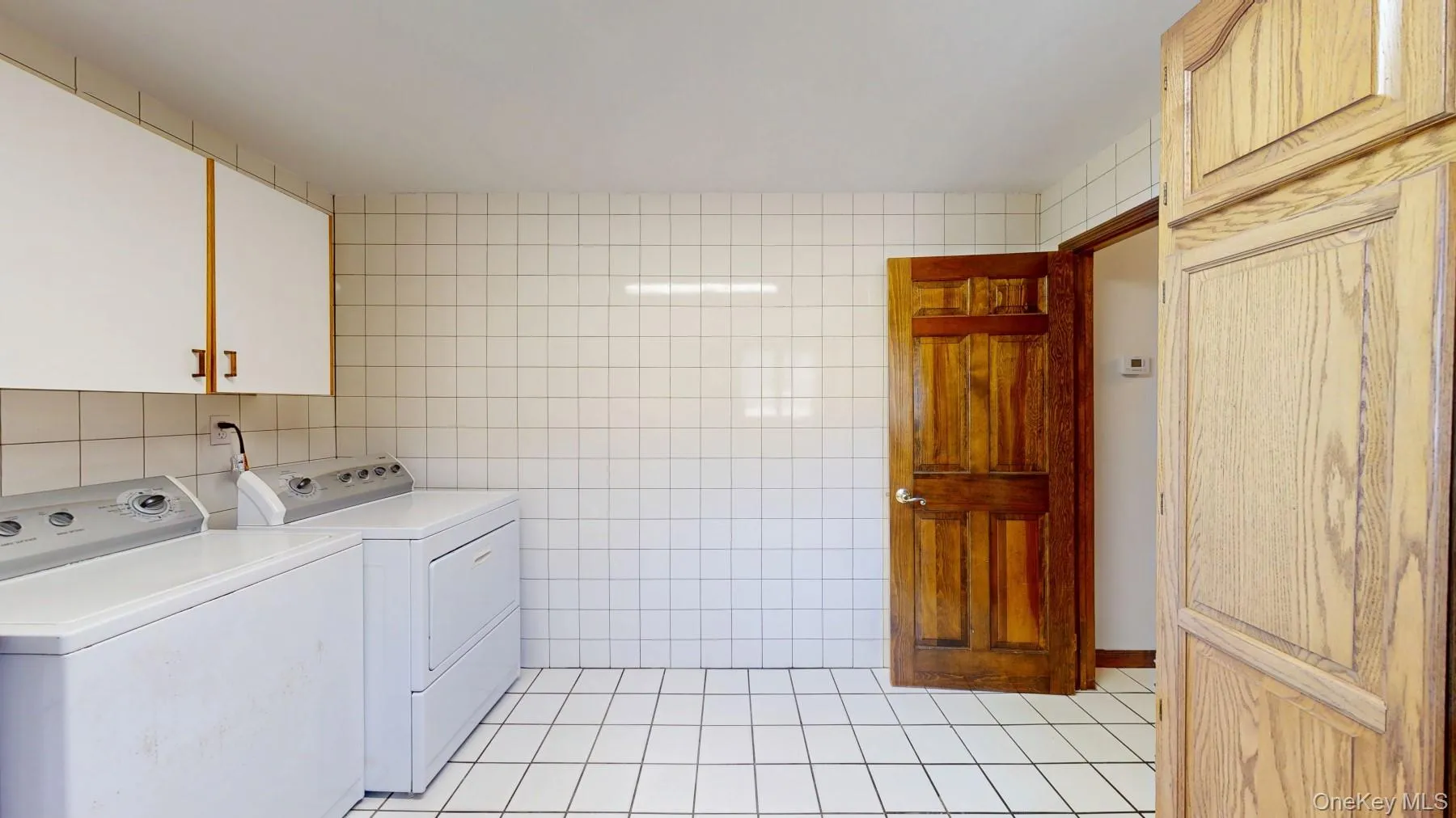 Laundry room featuring light tile patterned floors, washing machine and dryer, cabinet space, and tile walls Laundry room featuring light tile patterned floors, washing machine and dryer, cabinet space, and tile walls