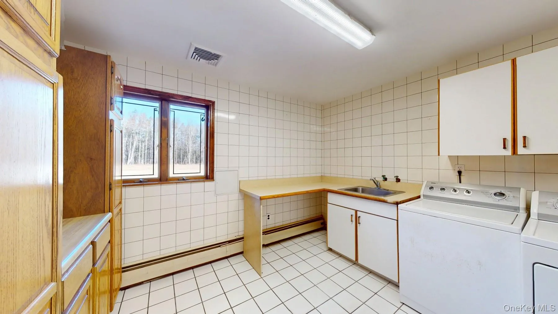 Laundry room featuring visible vents, cabinet space, a sink, washer and dryer, and tile walls Laundry room featuring visible vents, cabinet space, a sink, washer and dryer, and tile walls