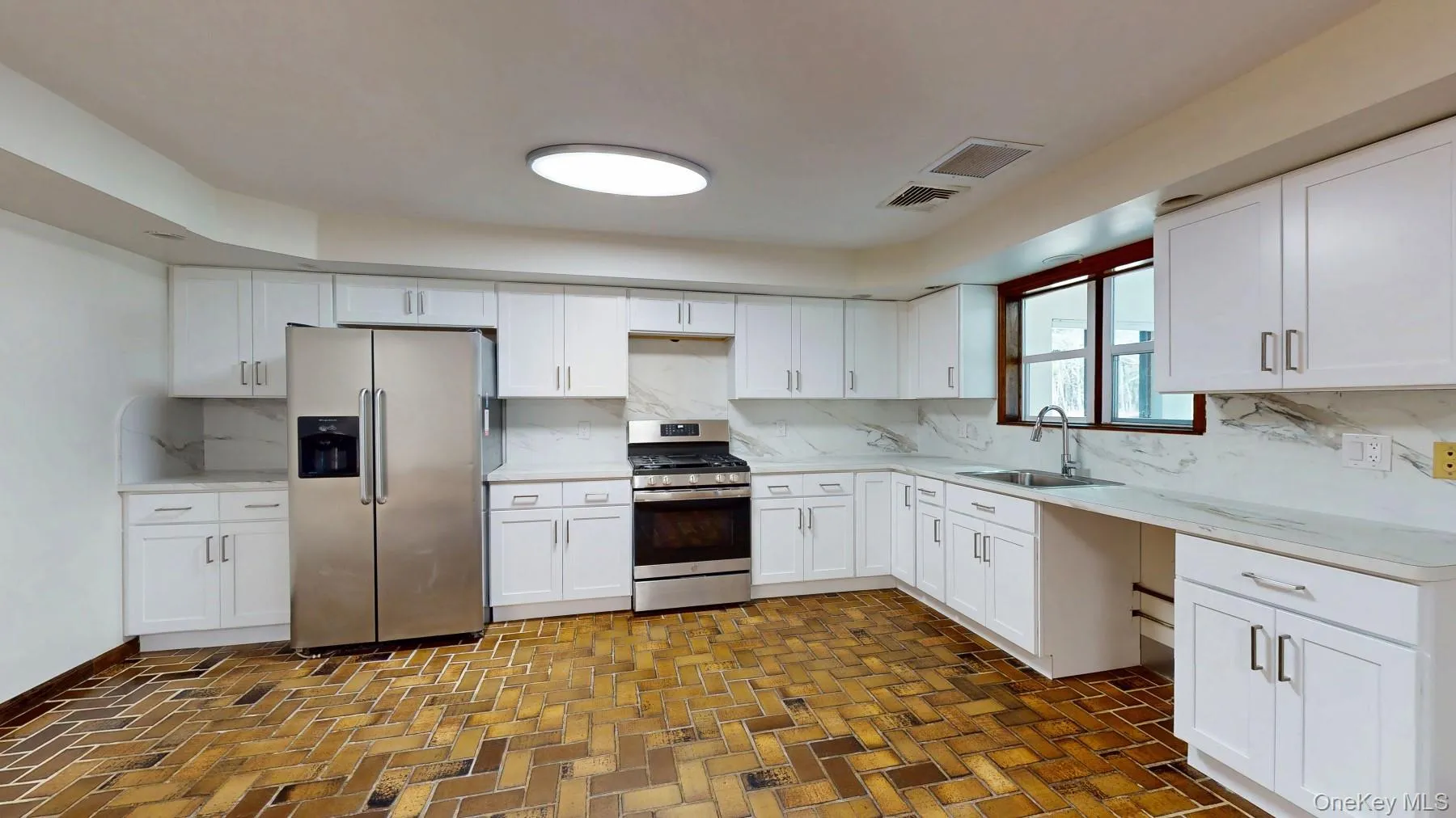 Kitchen with a sink, backsplash, appliances with stainless steel finishes, white cabinets, and brick floor Kitchen with a sink, backsplash, appliances with stainless steel finishes, white cabinets, and brick floor