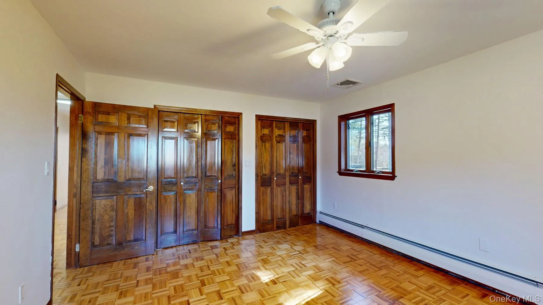 Unfurnished bedroom featuring baseboard heating, a ceiling fan, visible vents, and multiple closets Unfurnished bedroom featuring baseboard heating, a ceiling fan, visible vents, and multiple closets