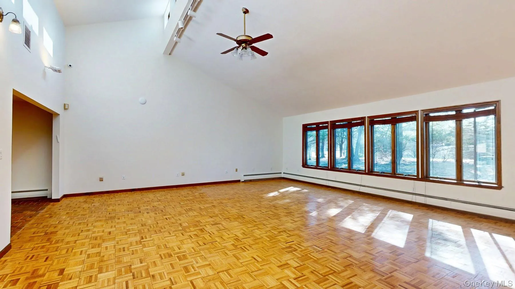 Unfurnished living room with ceiling fan, high vaulted ceiling, baseboards, and a baseboard radiator Unfurnished living room with ceiling fan, high vaulted ceiling, baseboards, and a baseboard radiator