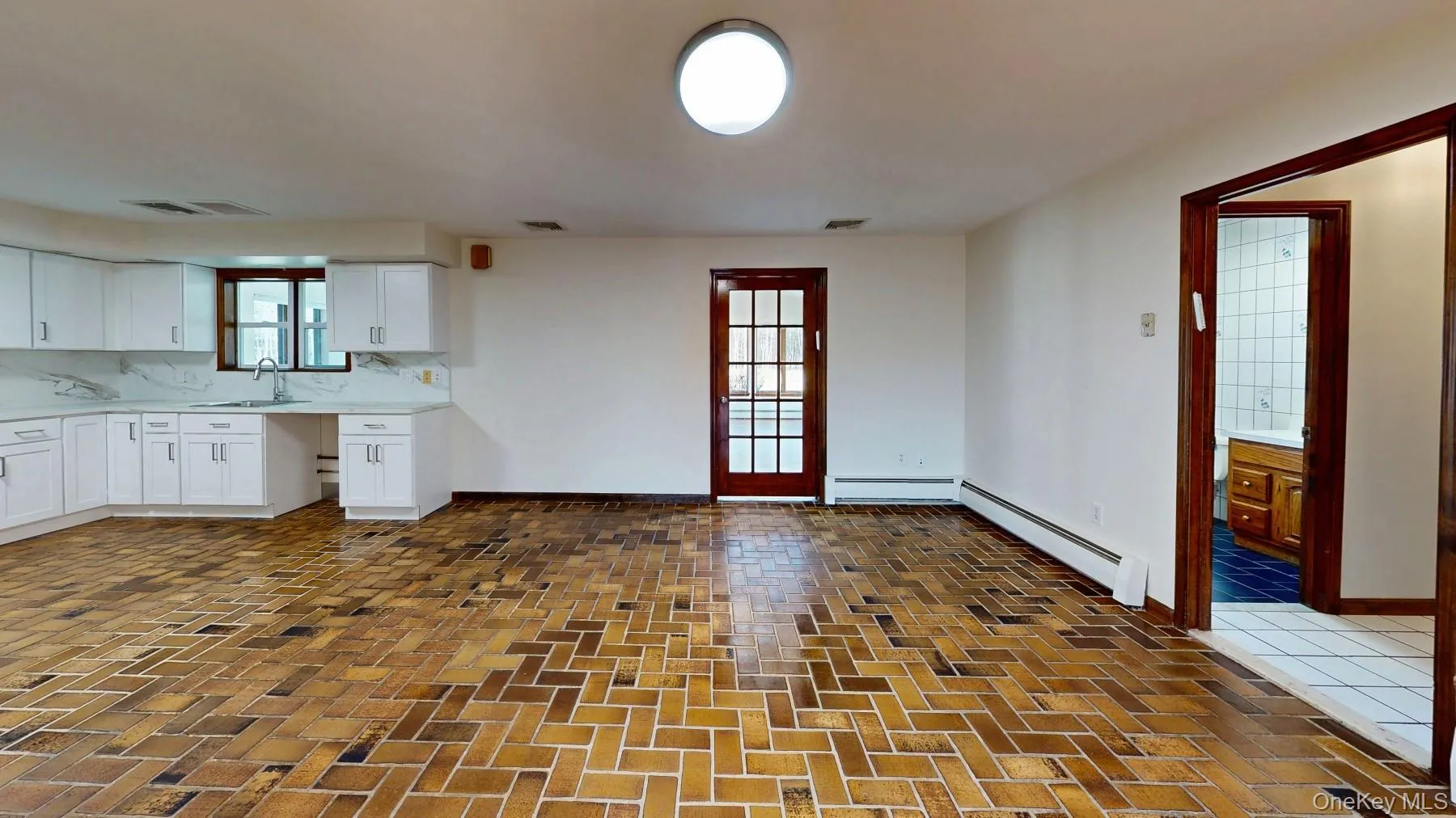Kitchen with visible vents, a baseboard radiator, a sink, light countertops, and white cabinetry Kitchen with visible vents, a baseboard radiator, a sink, light countertops, and white cabinetry