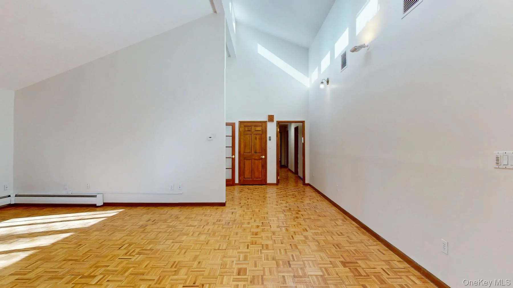 Unfurnished room with visible vents, baseboards, high vaulted ceiling, and baseboard heating Unfurnished room with visible vents, baseboards, high vaulted ceiling, and baseboard heating