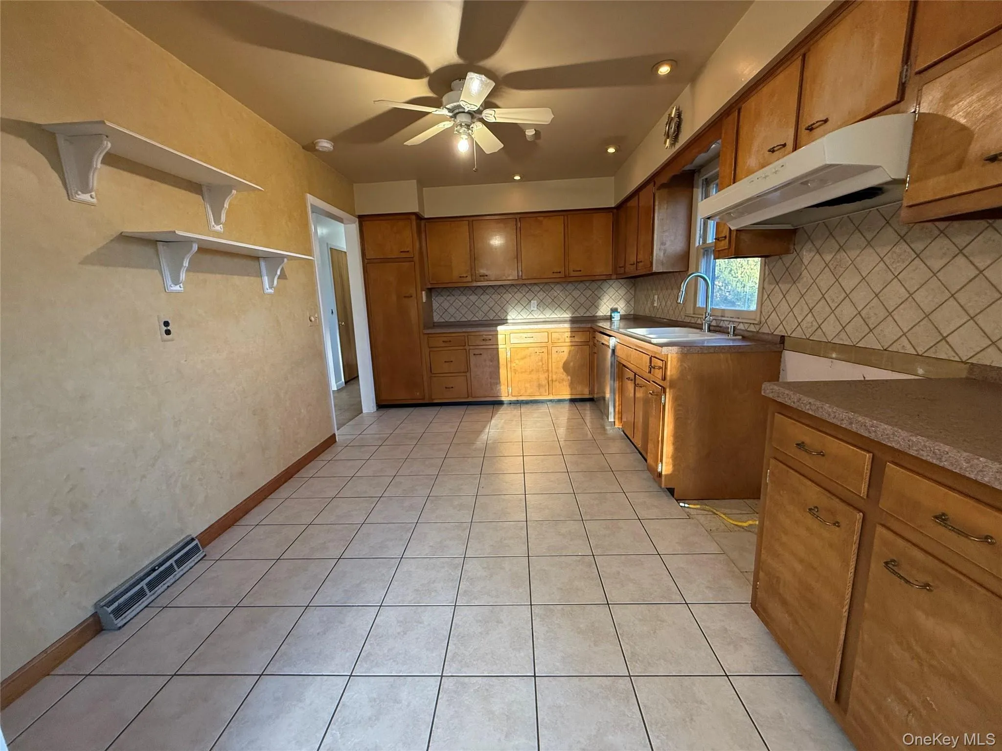 Kitchen featuring brown cabinetry, light tile patterned floors, under cabinet range hood, and tasteful backsplash Kitchen featuring brown cabinetry, light tile patterned floors, under cabinet range hood, and tasteful backsplash