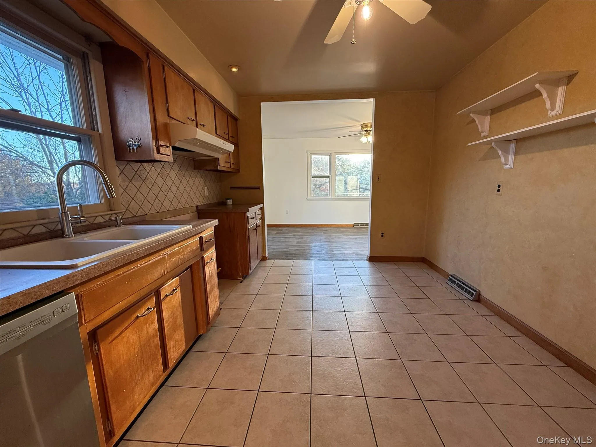 Kitchen with stainless steel dishwasher, brown cabinets, tasteful backsplash, light tile patterned floors, and recessed lighting Kitchen with stainless steel dishwasher, brown cabinets, tasteful backsplash, light tile patterned floors, and recessed lighting