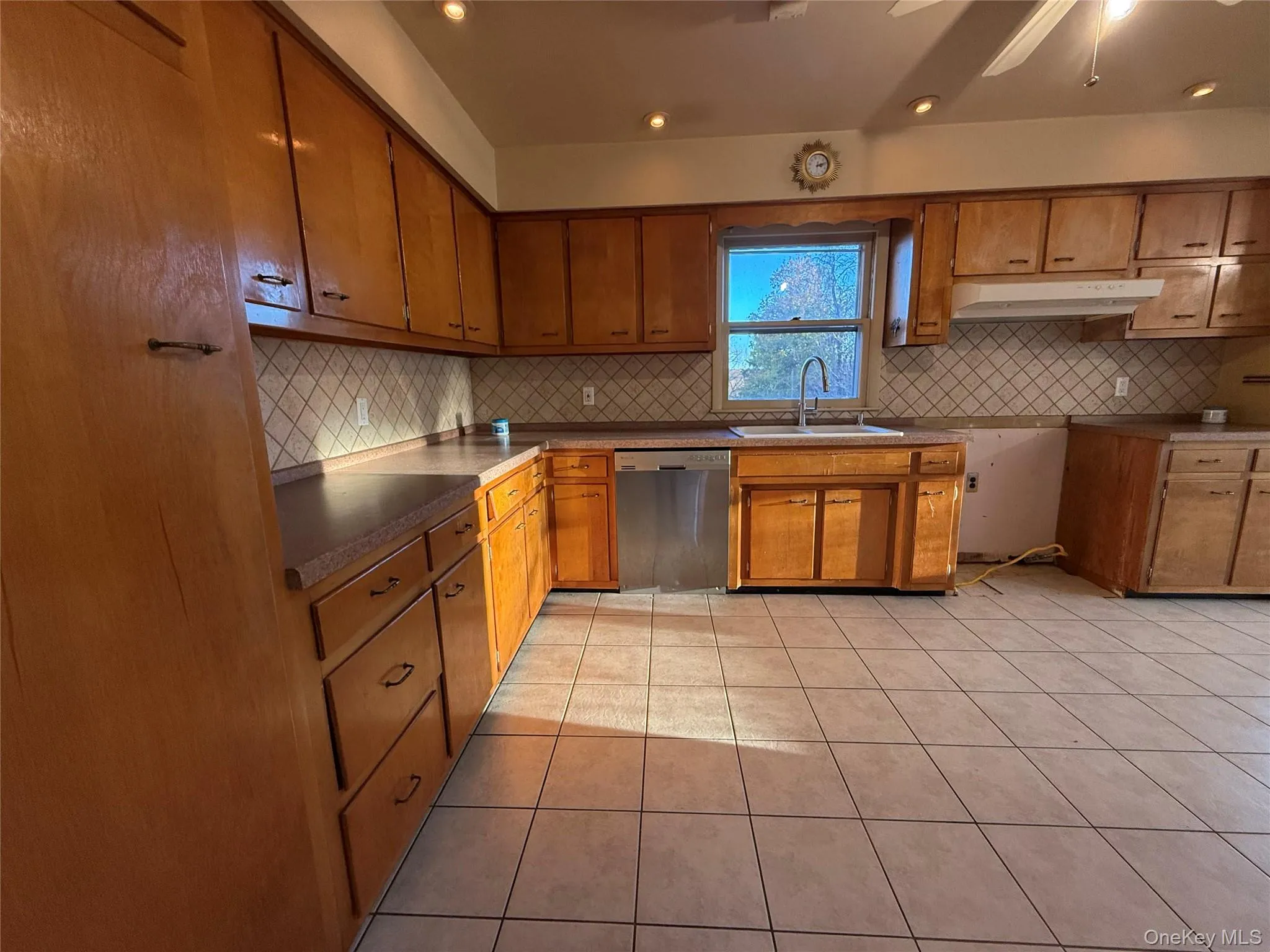Kitchen featuring light tile patterned flooring, brown cabinets, dishwasher, tasteful backsplash, and recessed lighting Kitchen featuring light tile patterned flooring, brown cabinets, dishwasher, tasteful backsplash, and recessed lighting