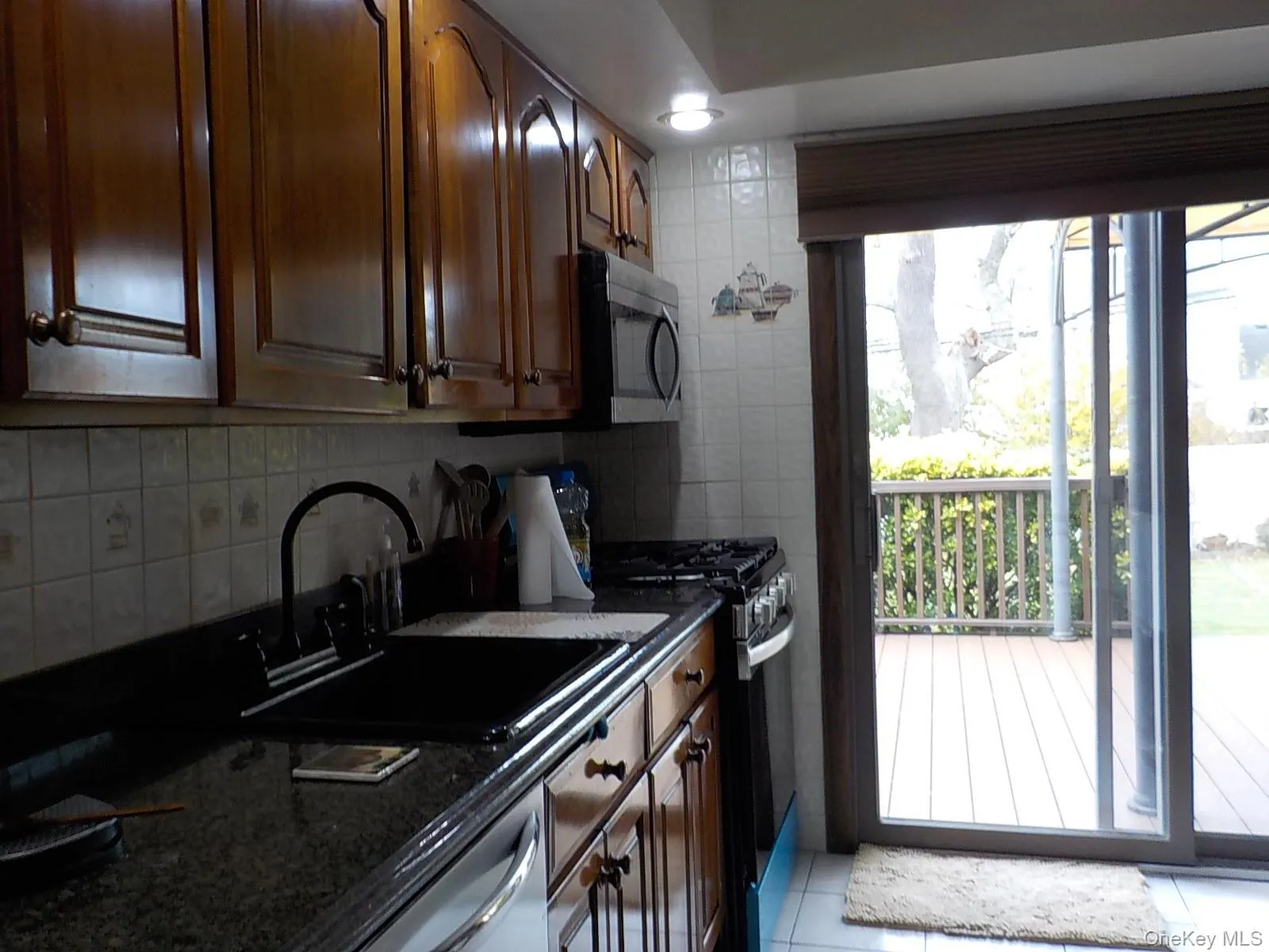 Kitchen featuring stainless steel appliances, dark stone counters, light tile patterned flooring, tasteful backsplash, and tile walls Kitchen featuring stainless steel appliances, dark stone counters, light tile patterned flooring, tasteful backsplash, and tile walls