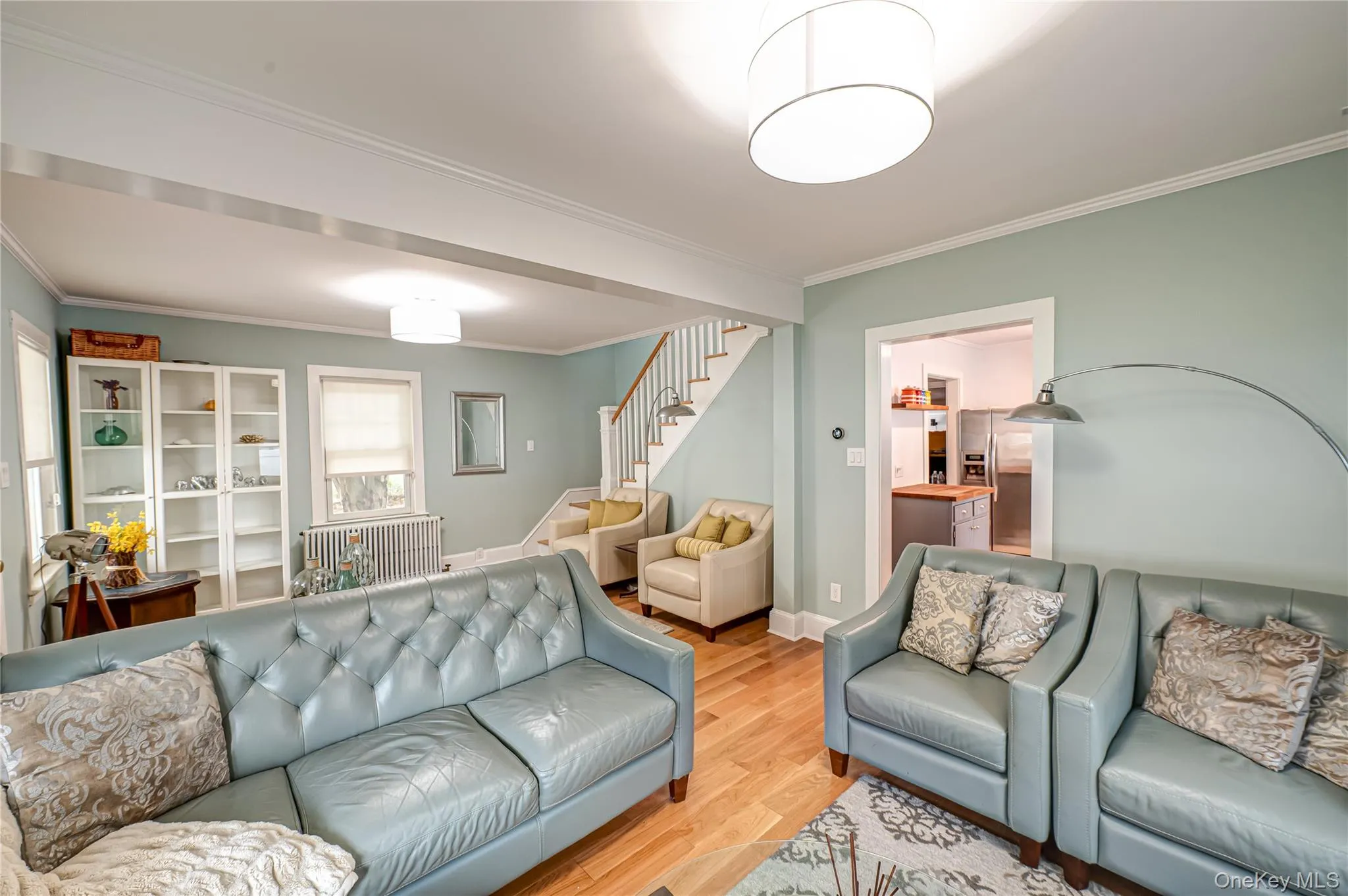 Living room with crown molding, wood finished floors, stairs, and radiator Living room with crown molding, wood finished floors, stairs, and radiator