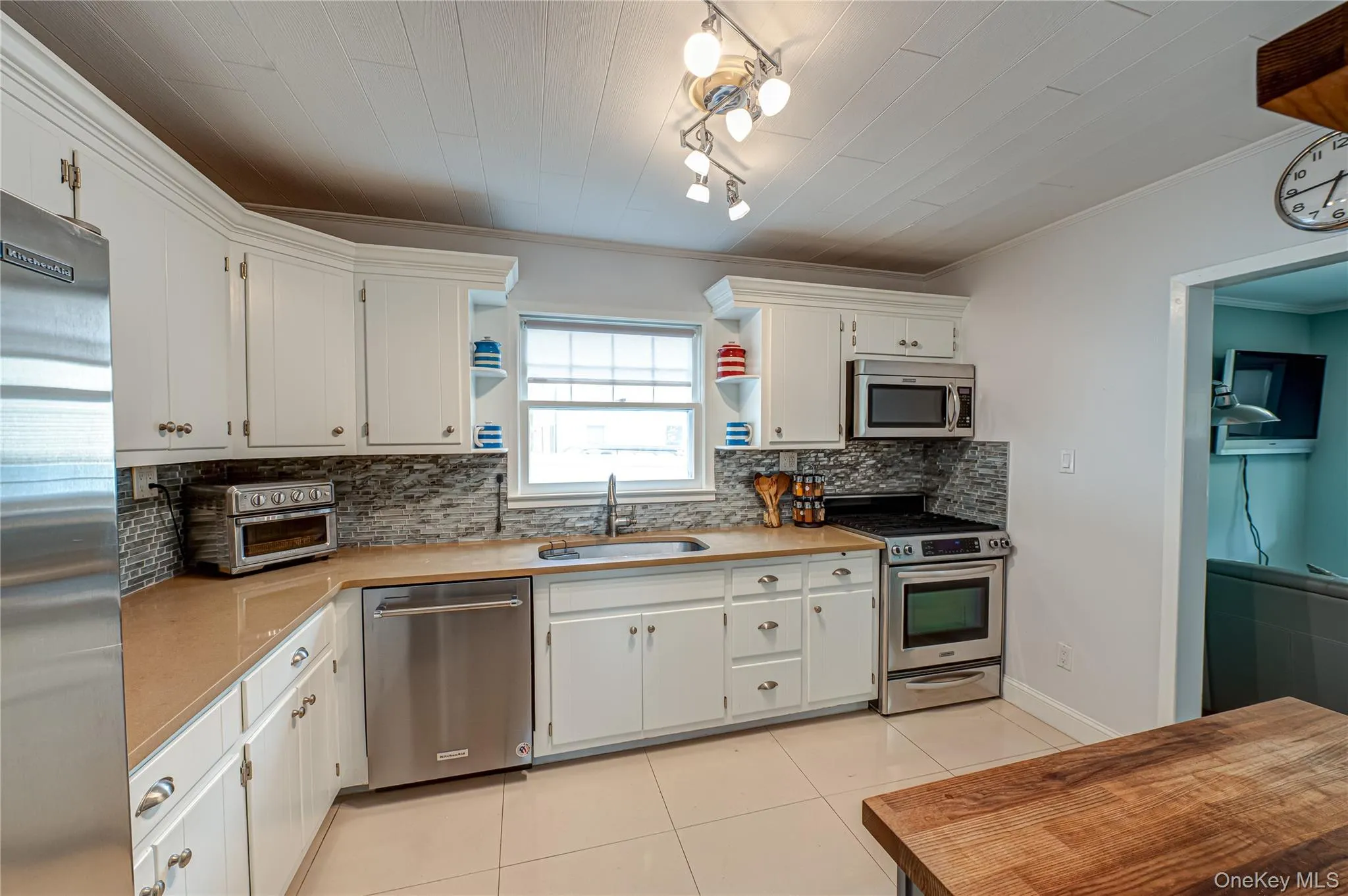 Kitchen featuring light countertops, light tile patterned floors, stainless steel appliances, backsplash, and ornamental molding Kitchen featuring light countertops, light tile patterned floors, stainless steel appliances, backsplash, and ornamental molding