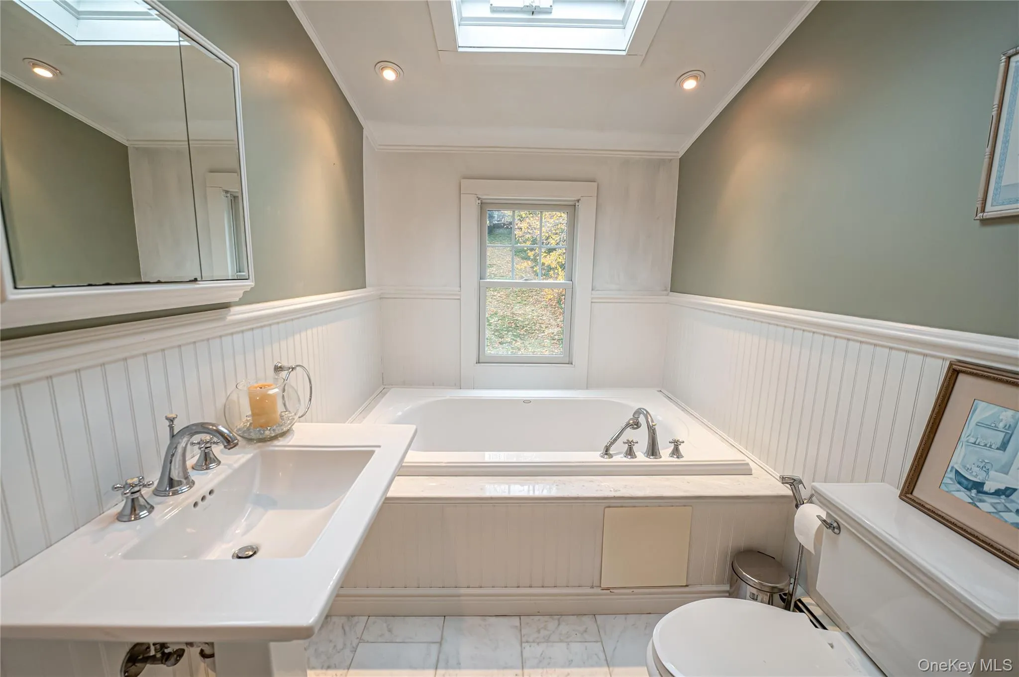 Full bathroom with a skylight, a bath, crown molding, recessed lighting, and a wainscoted wall Full bathroom with a skylight, a bath, crown molding, recessed lighting, and a wainscoted wall