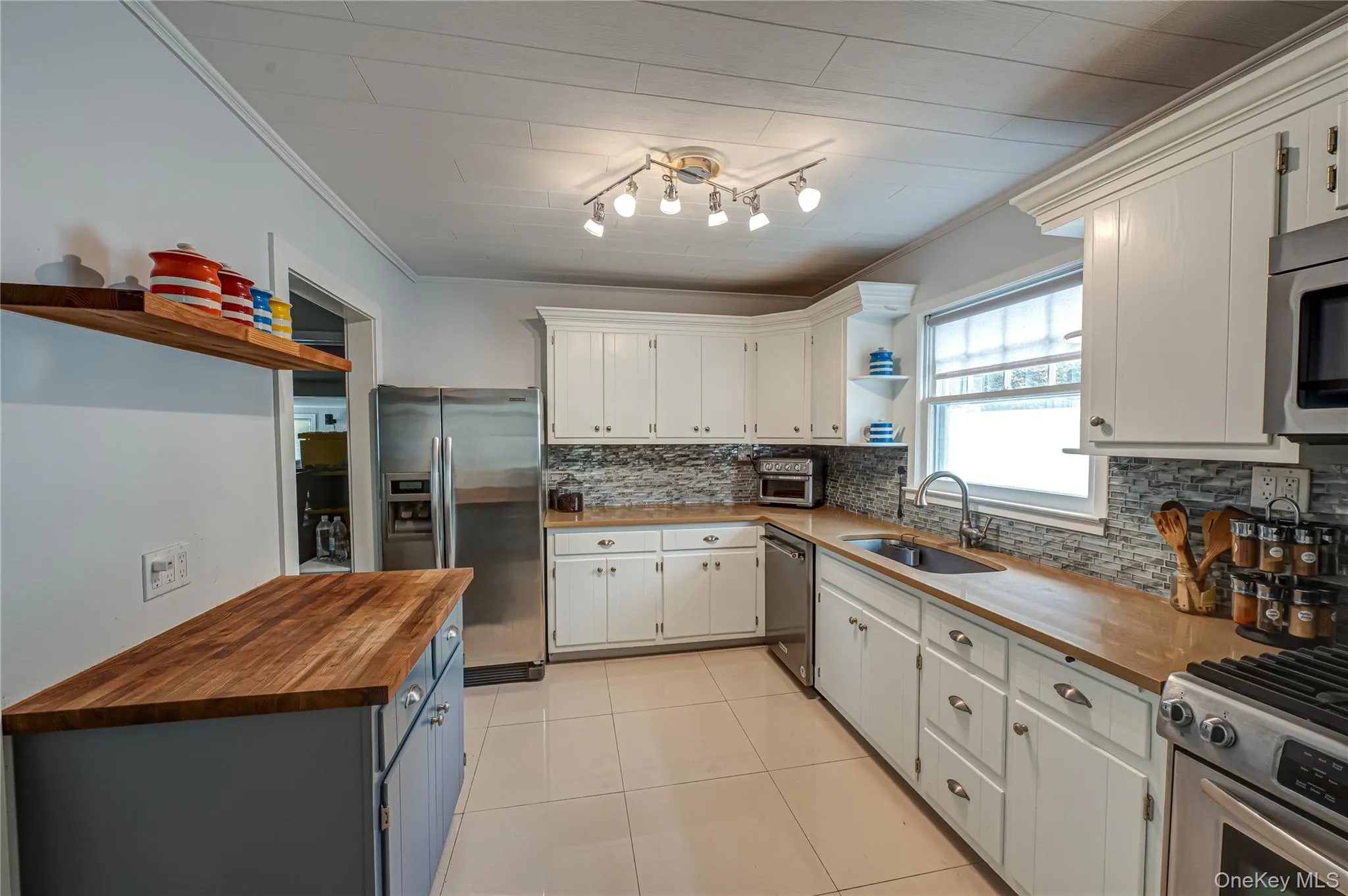 Kitchen featuring wood counters, ornamental molding, decorative backsplash, stainless steel appliances, and open shelves Kitchen featuring wood counters, ornamental molding, decorative backsplash, stainless steel appliances, and open shelves