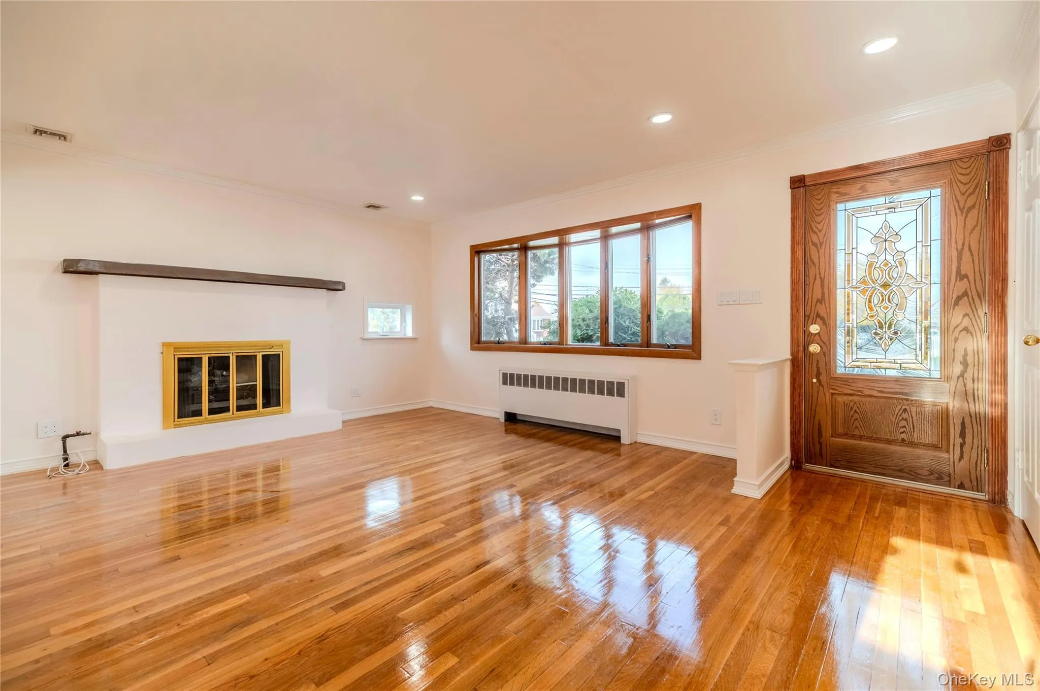 Unfurnished living room with ornamental molding, radiator, light wood-style flooring, a glass covered fireplace, and recessed lighting Unfurnished living room with ornamental molding, radiator, light wood-style flooring, a glass covered fireplace, and recessed lighting
