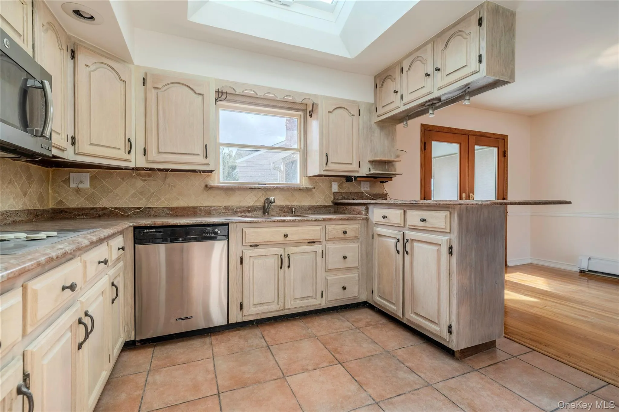 Kitchen featuring backsplash, appliances with stainless steel finishes, light tile patterned floors, a peninsula, and light brown cabinetry Kitchen featuring backsplash, appliances with stainless steel finishes, light tile patterned floors, a peninsula, and light brown cabinetry