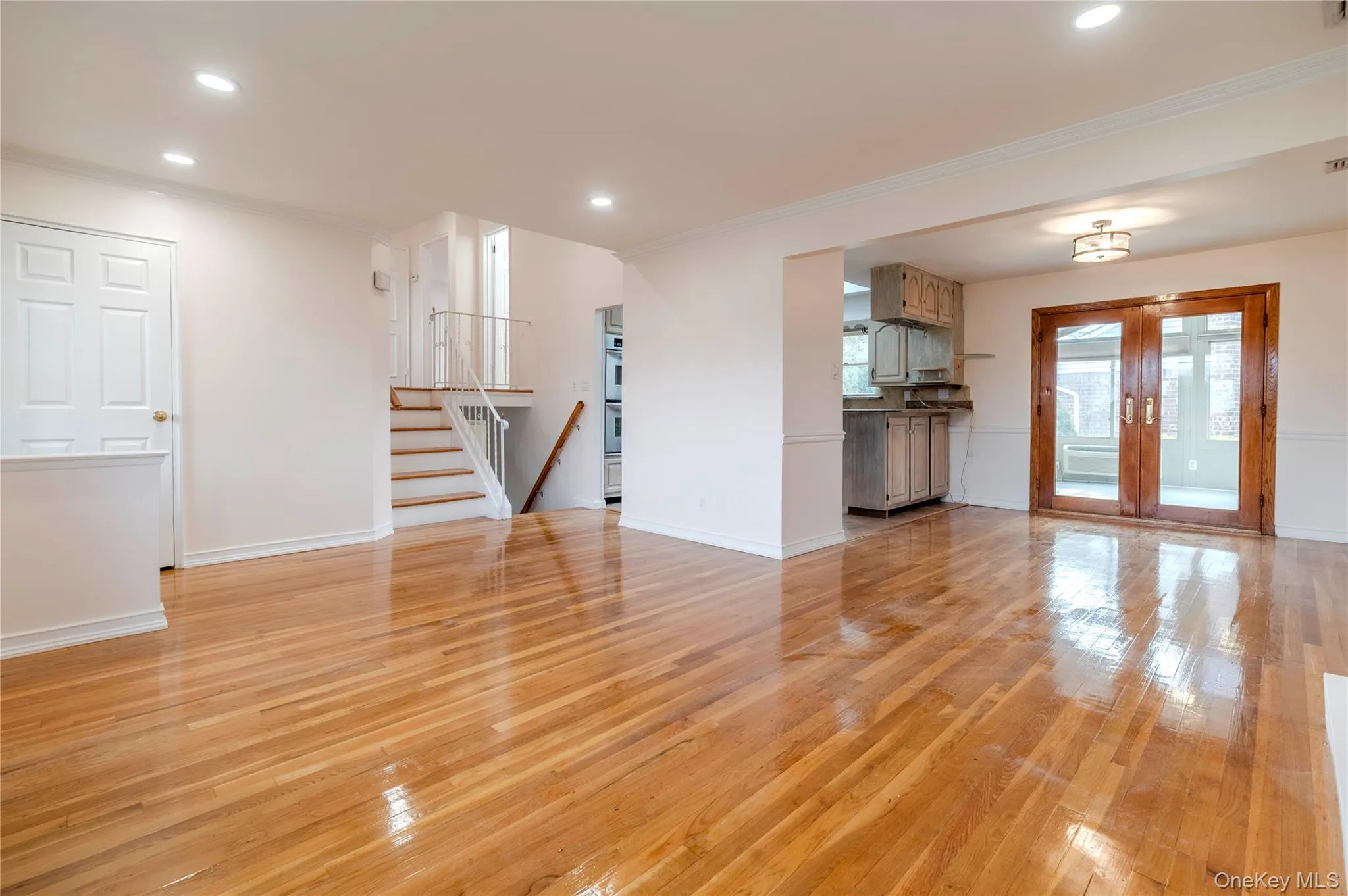 Unfurnished living room featuring light wood-style floors, recessed lighting, crown molding, french doors, and stairs Unfurnished living room featuring light wood-style floors, recessed lighting, crown molding, french doors, and stairs