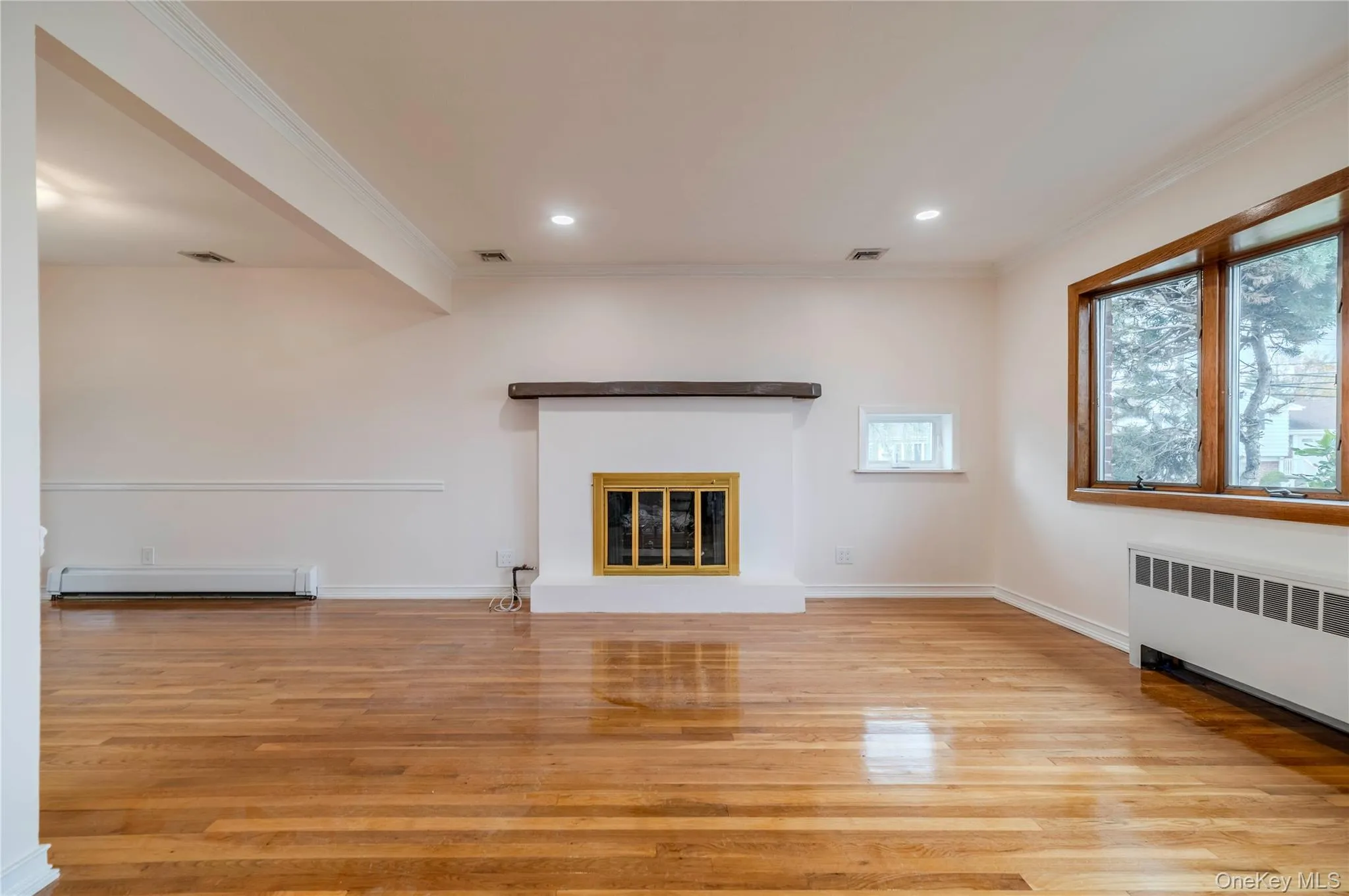 Unfurnished living room with crown molding, light wood-style flooring, a glass covered fireplace, baseboard heating, and recessed lighting Unfurnished living room with crown molding, light wood-style flooring, a glass covered fireplace, baseboard heating, and recessed lighting