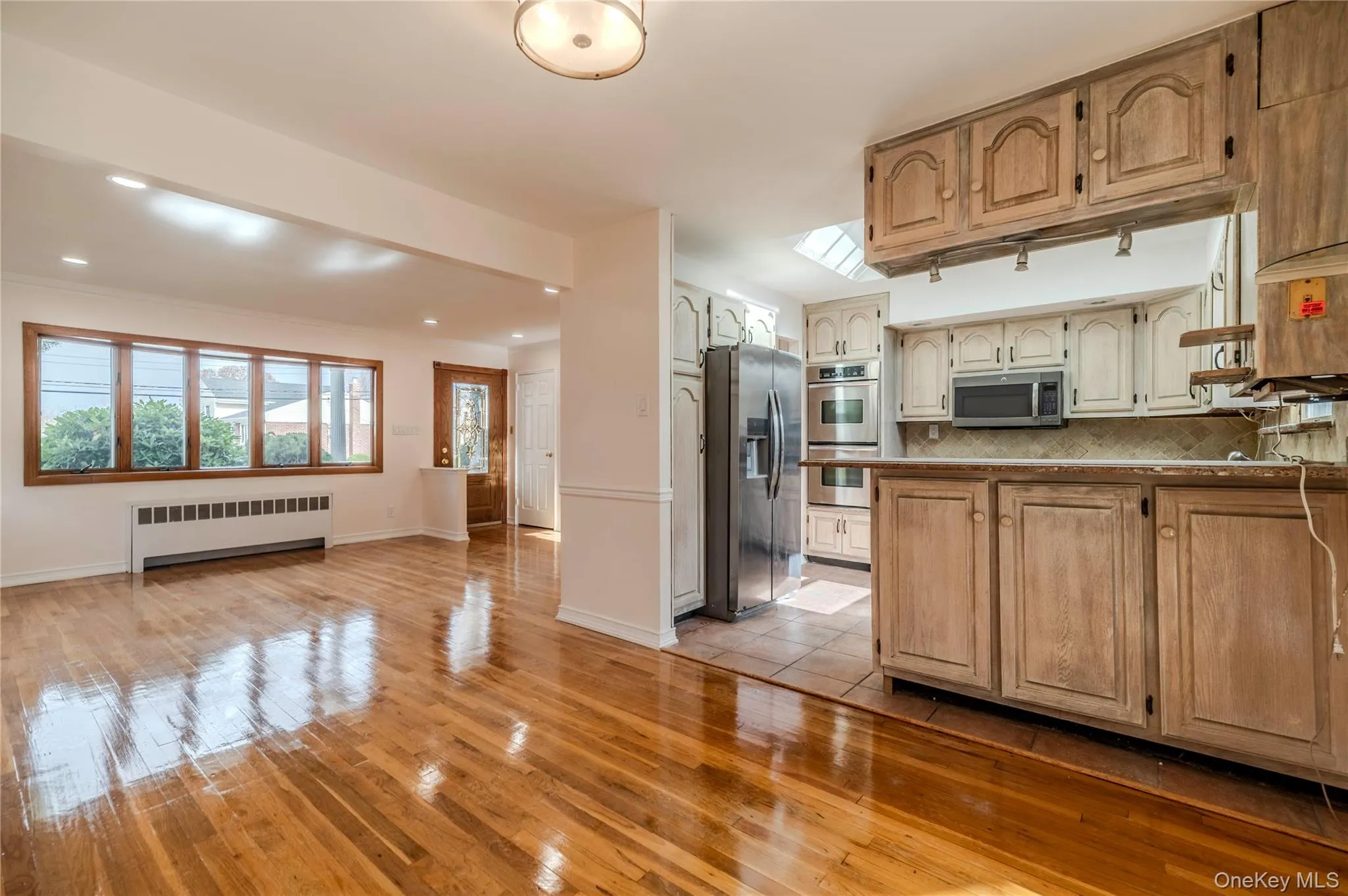 Kitchen featuring light wood-type flooring, radiator, stainless steel appliances, tasteful backsplash, and open floor plan Kitchen featuring light wood-type flooring, radiator, stainless steel appliances, tasteful backsplash, and open floor plan