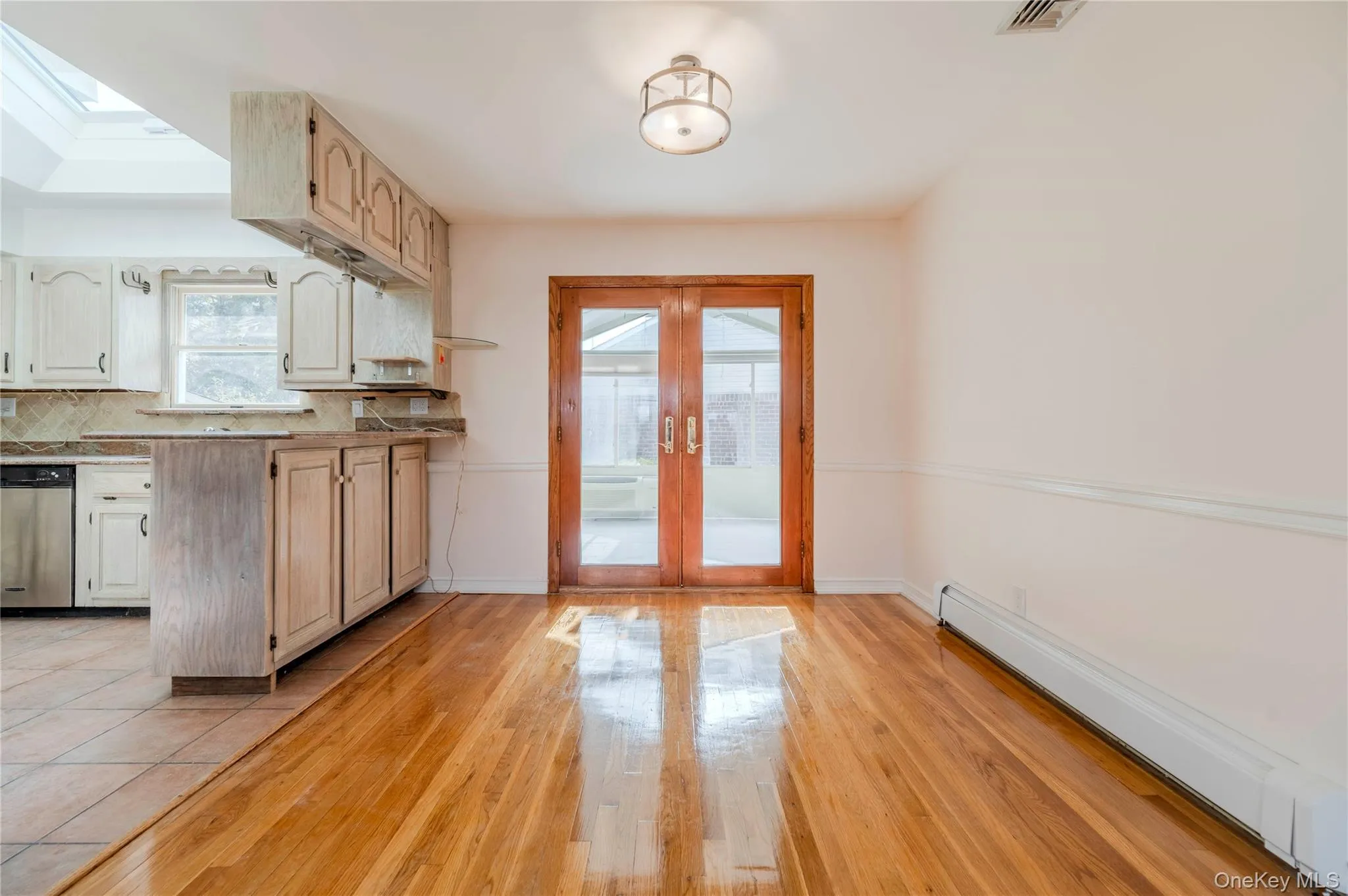 Kitchen featuring baseboard heating, french doors, tasteful backsplash, stainless steel dishwasher, and light wood-style flooring Kitchen featuring baseboard heating, french doors, tasteful backsplash, stainless steel dishwasher, and light wood-style flooring