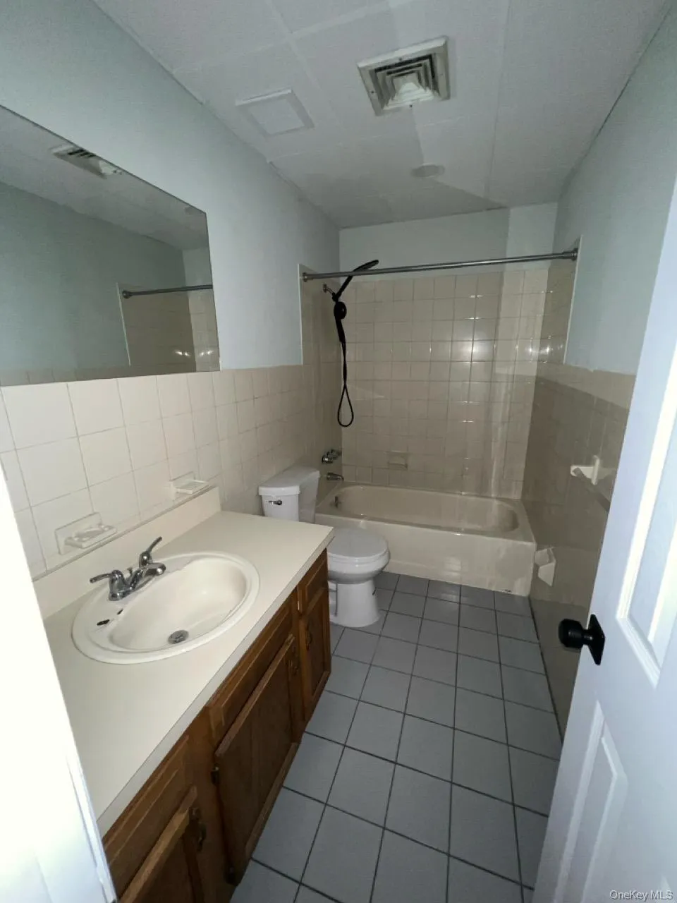 Bathroom featuring tile walls, bathtub / shower combination, dark tile patterned floors, vanity, and decorative backsplash Bathroom featuring tile walls, bathtub / shower combination, dark tile patterned floors, vanity, and decorative backsplash