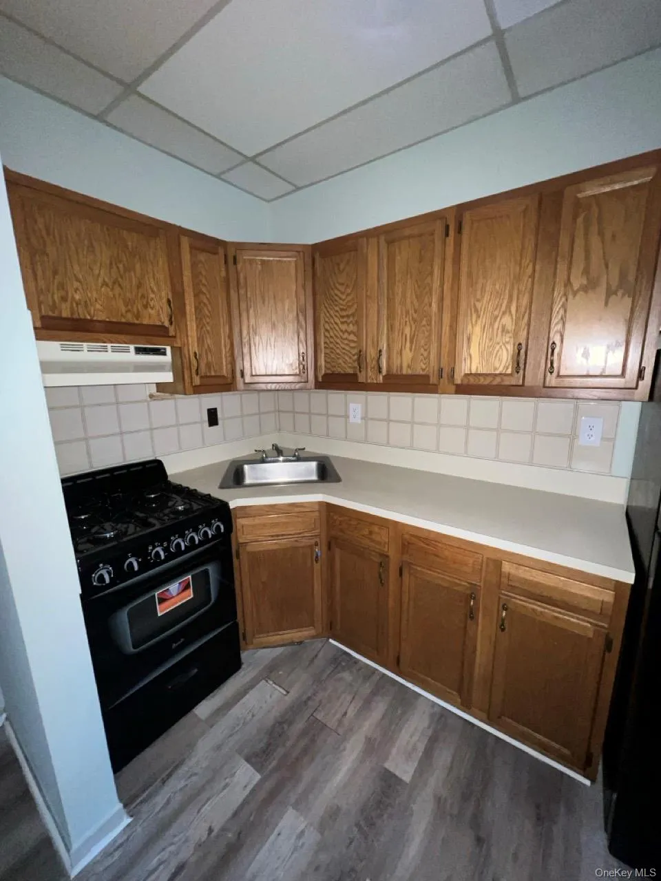 Kitchen with brown cabinets, a drop ceiling, gas stove, and light countertops Kitchen with brown cabinets, a drop ceiling, gas stove, and light countertops