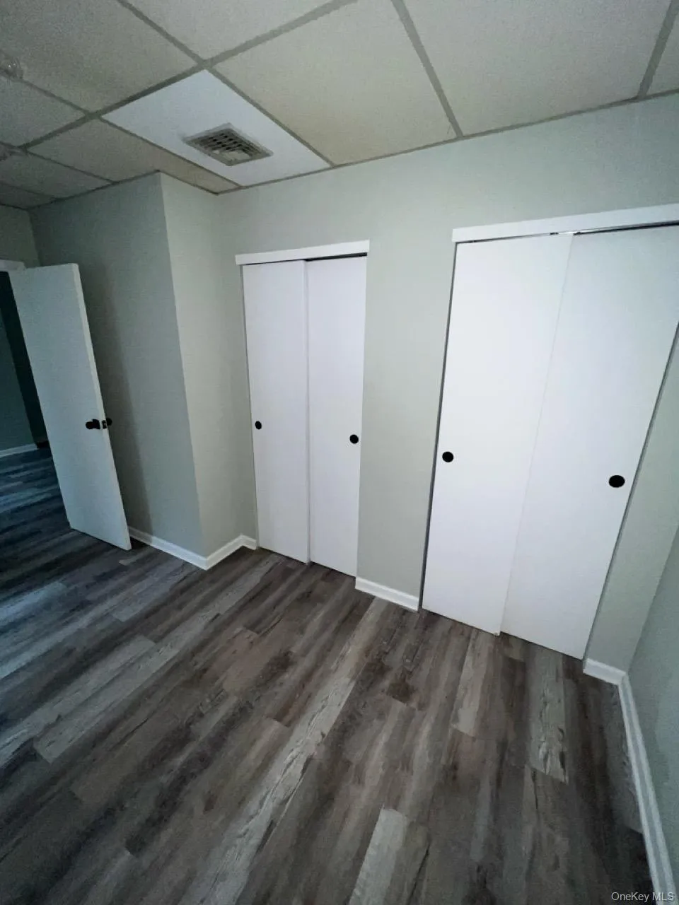 Unfurnished bedroom with a paneled ceiling, multiple closets, and dark wood-style floors Unfurnished bedroom with a paneled ceiling, multiple closets, and dark wood-style floors