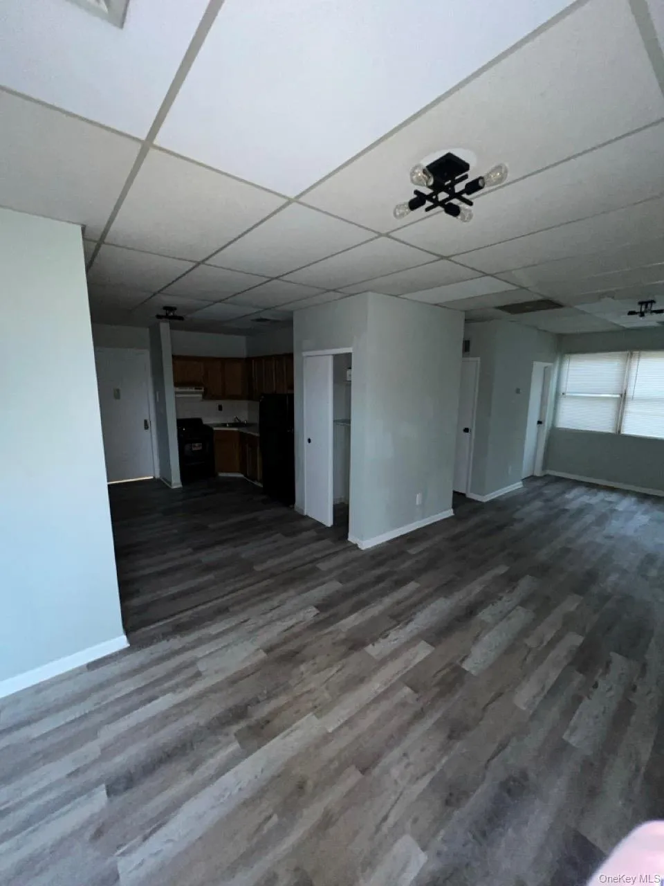 Unfurnished living room featuring dark wood-type flooring and a paneled ceiling Unfurnished living room featuring dark wood-type flooring and a paneled ceiling