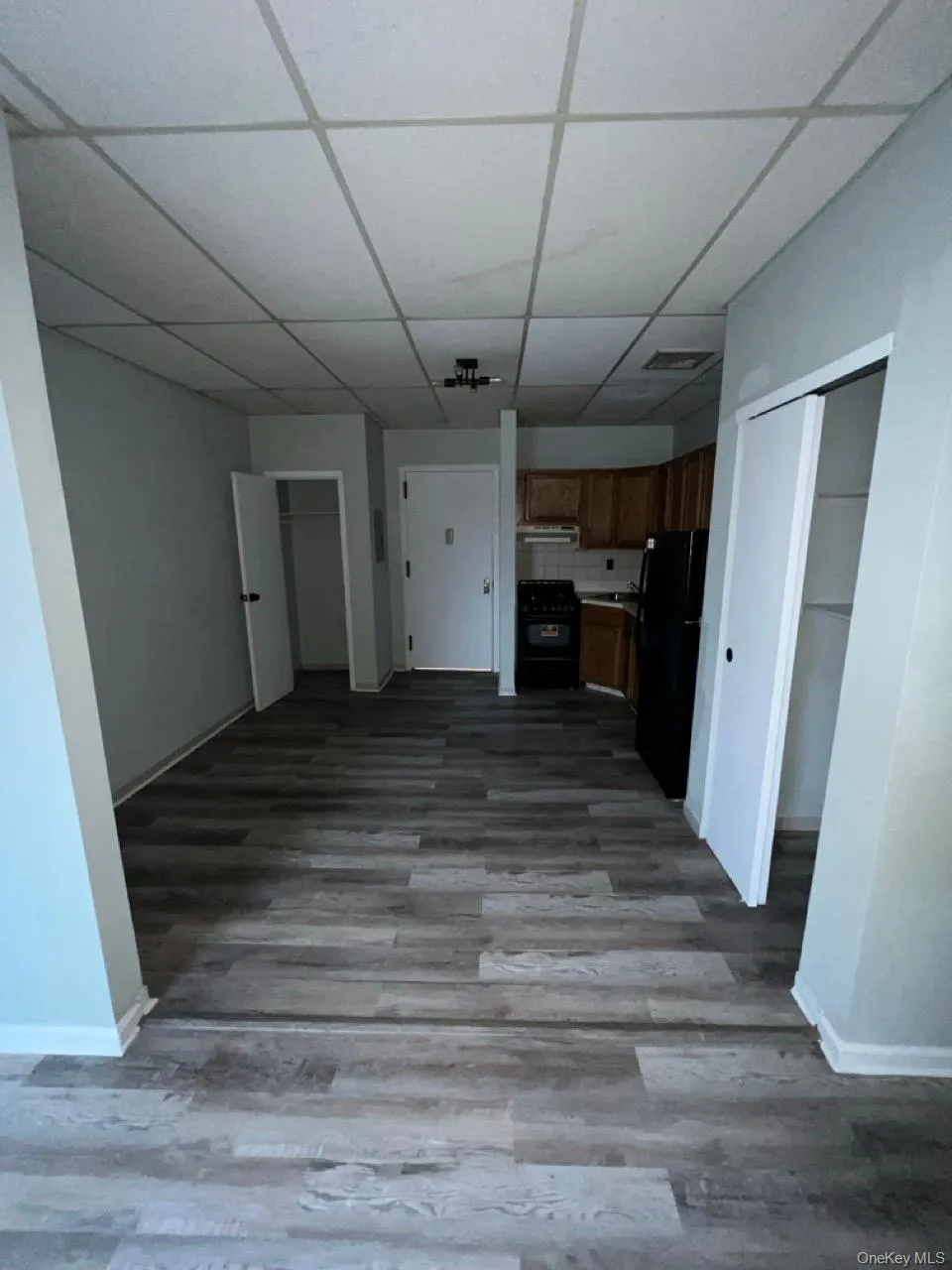 Unfurnished living room with dark wood-style flooring and a paneled ceiling Unfurnished living room with dark wood-style flooring and a paneled ceiling