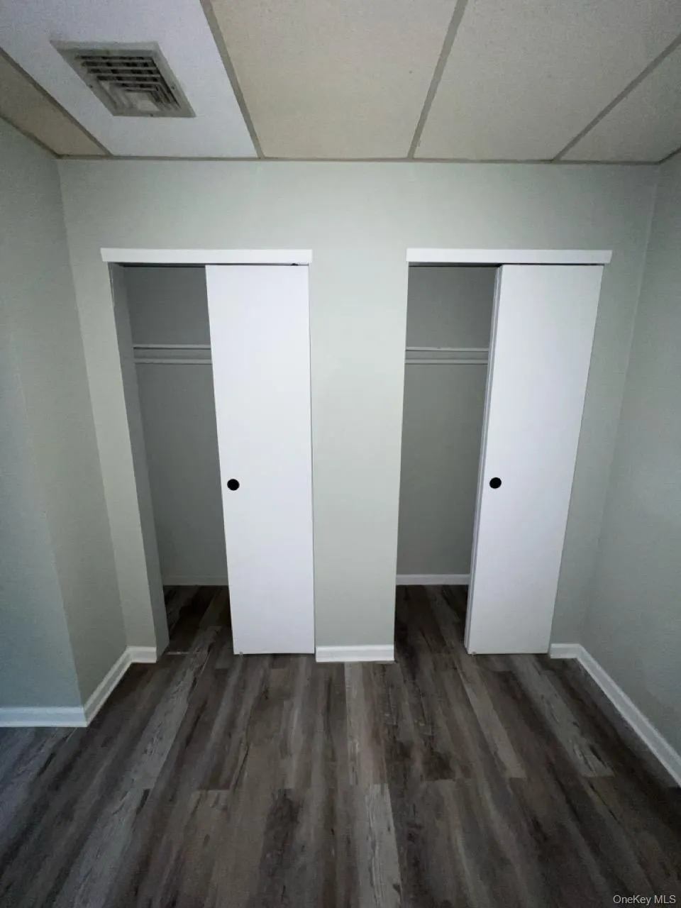 Unfurnished bedroom with a paneled ceiling, multiple closets, and dark wood-style floors Unfurnished bedroom with a paneled ceiling, multiple closets, and dark wood-style floors