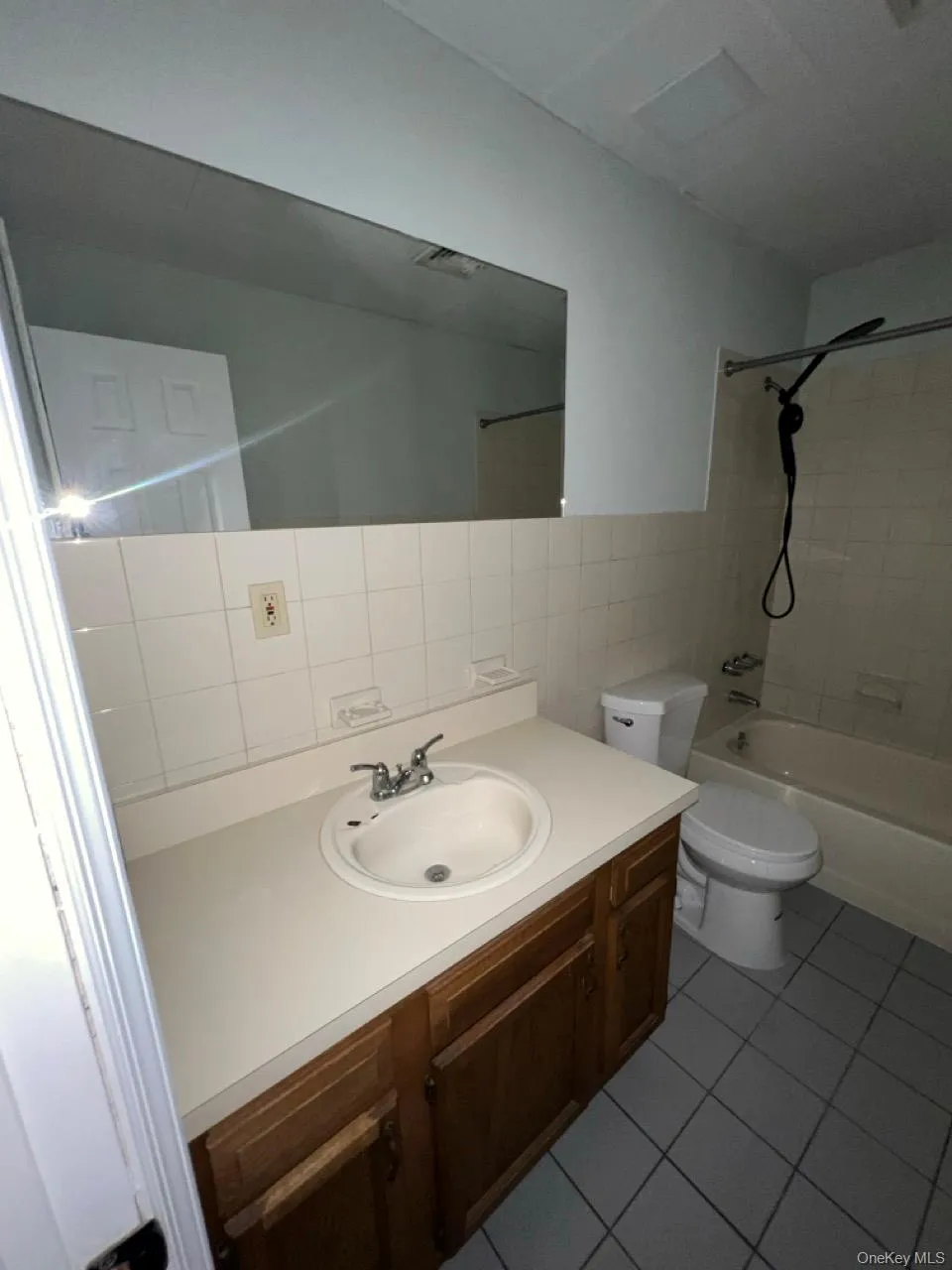 Full bath featuring tile walls, shower / bathtub combination, vanity, and dark tile patterned flooring Full bath featuring tile walls, shower / bathtub combination, vanity, and dark tile patterned flooring