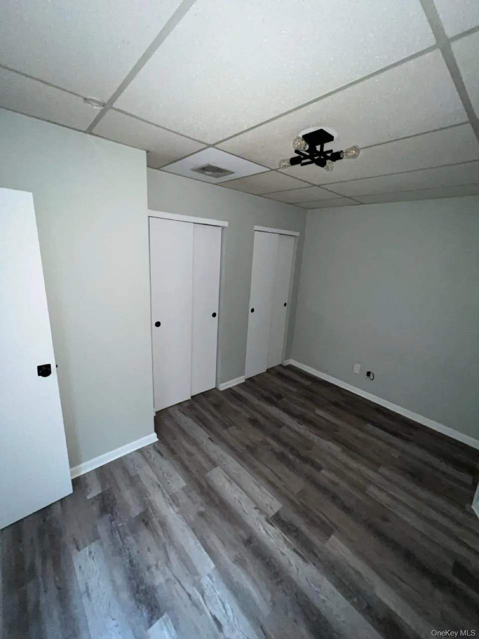 Unfurnished bedroom featuring a paneled ceiling, multiple closets, and dark wood-type flooring Unfurnished bedroom featuring a paneled ceiling, multiple closets, and dark wood-type flooring
