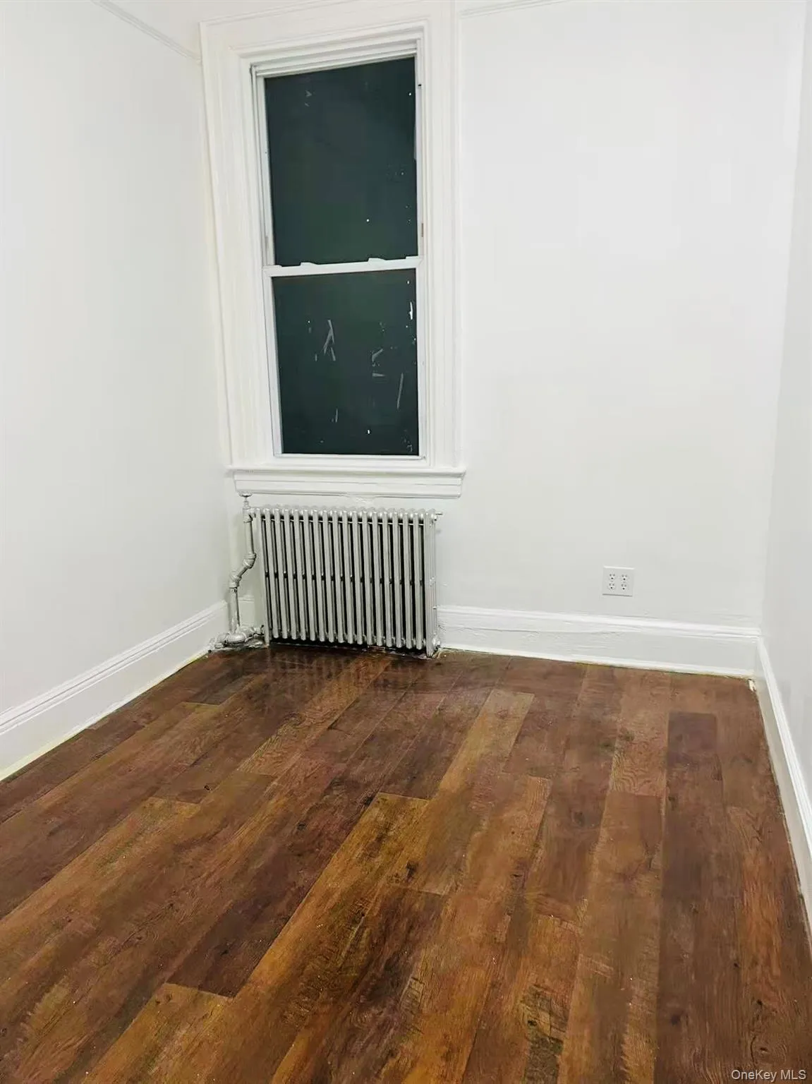 Unfurnished room with dark wood-style floors and radiator Unfurnished room with dark wood-style floors and radiator