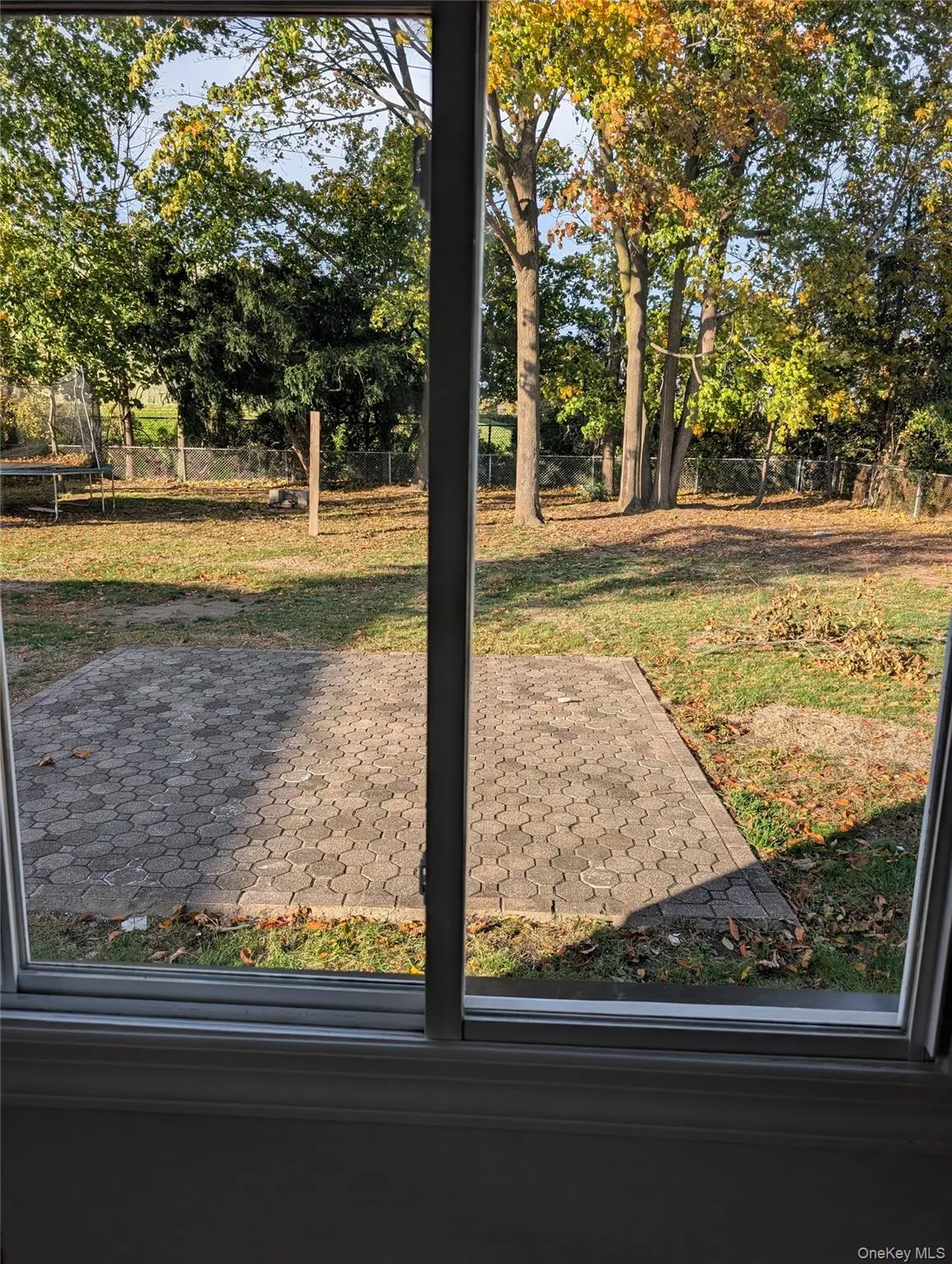 Fenced backyard with a trampoline, a patio area, and view of scattered trees Fenced backyard with a trampoline, a patio area, and view of scattered trees