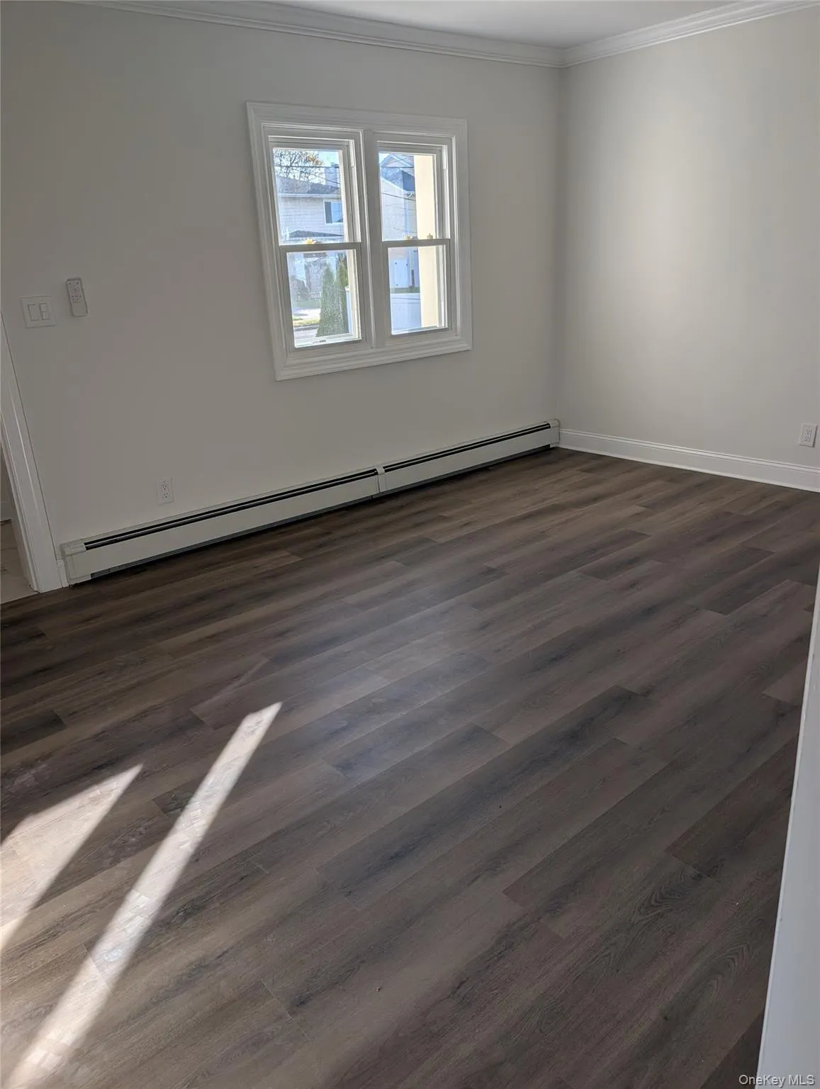 Spare room featuring baseboard heating, dark wood-type flooring, and ornamental molding Spare room featuring baseboard heating, dark wood-type flooring, and ornamental molding