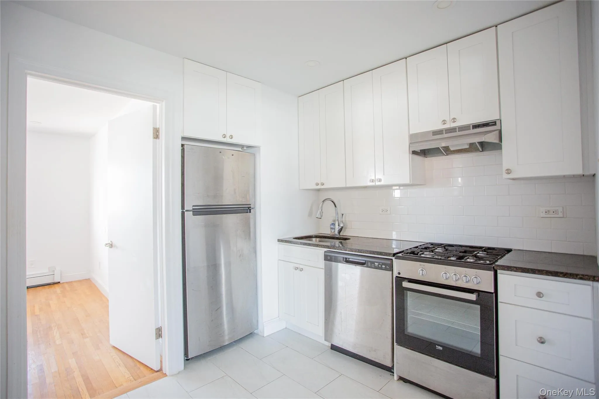 Kitchen featuring appliances with stainless steel finishes, white cabinets, tasteful backsplash, under cabinet range hood, and dark stone countertops Kitchen featuring appliances with stainless steel finishes, white cabinets, tasteful backsplash, under cabinet range hood, and dark stone countertops