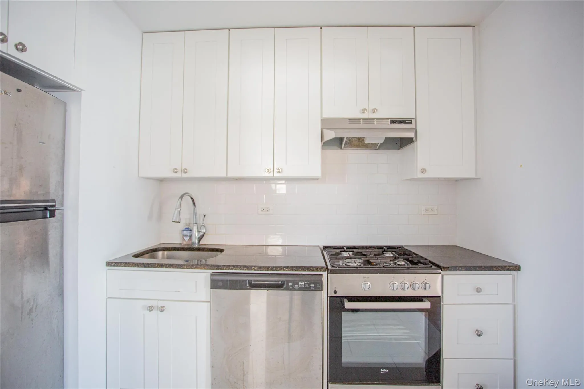 Kitchen with stainless steel dishwasher, range with gas stovetop, freestanding refrigerator, white cabinetry, and tasteful backsplash Kitchen with stainless steel dishwasher, range with gas stovetop, freestanding refrigerator, white cabinetry, and tasteful backsplash