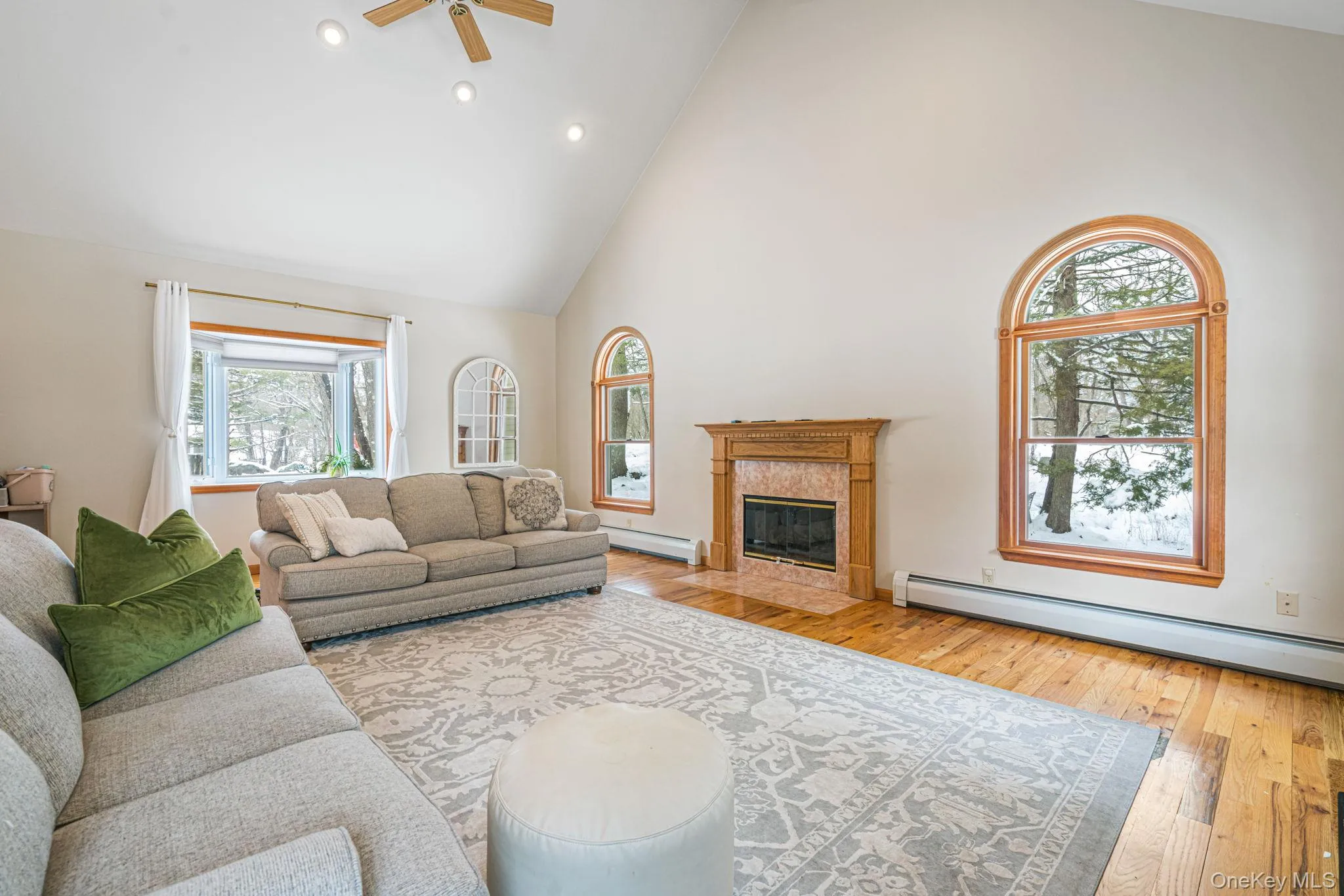 Living area with high vaulted ceiling, recessed lighting, light wood-style flooring, baseboard heating, and a premium fireplace Living area with high vaulted ceiling, recessed lighting, light wood-style flooring, baseboard heating, and a premium fireplace