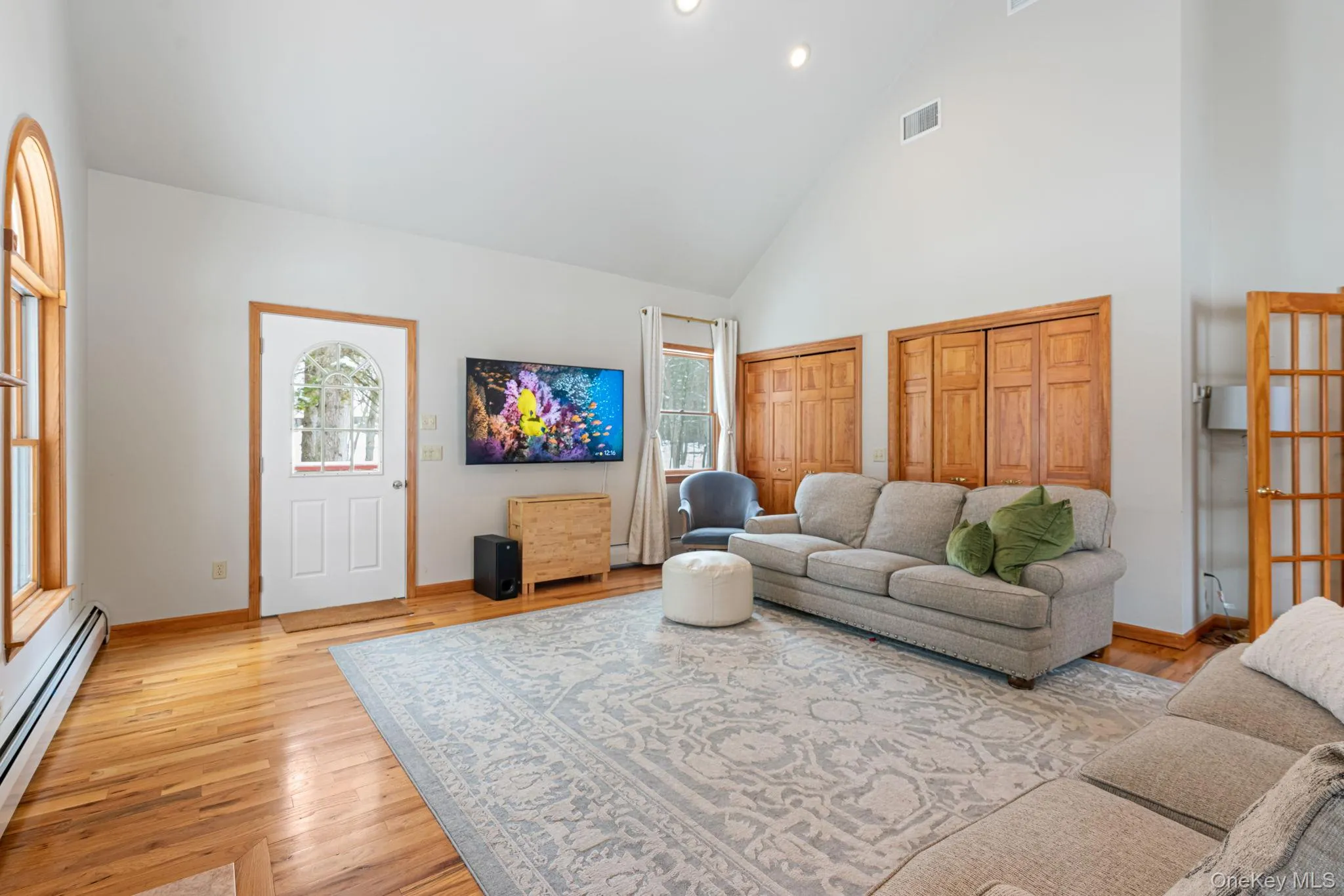 Living area featuring high vaulted ceiling, baseboard heating, light wood-style flooring, and recessed lighting Living area featuring high vaulted ceiling, baseboard heating, light wood-style flooring, and recessed lighting