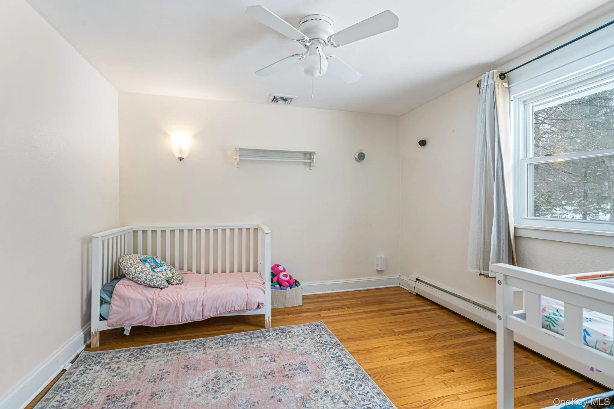 Bedroom with light wood-type flooring, ceiling fan, and a baseboard heating unit Bedroom with light wood-type flooring, ceiling fan, and a baseboard heating unit