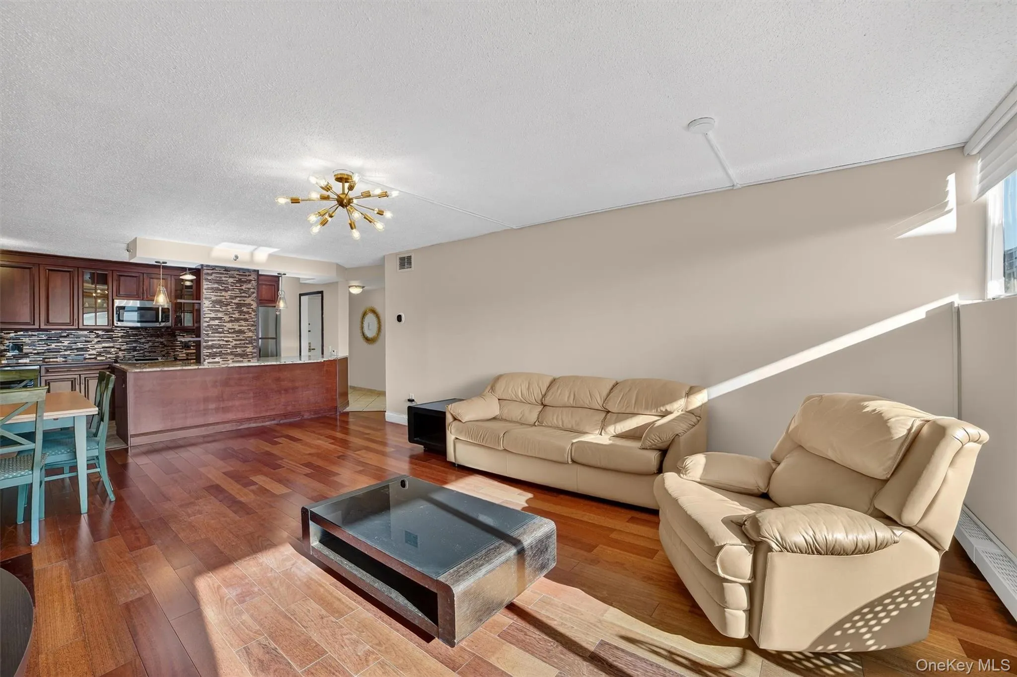 Living room with a textured ceiling, a baseboard heating unit, wood finished floors, and a chandelier Living room with a textured ceiling, a baseboard heating unit, wood finished floors, and a chandelier