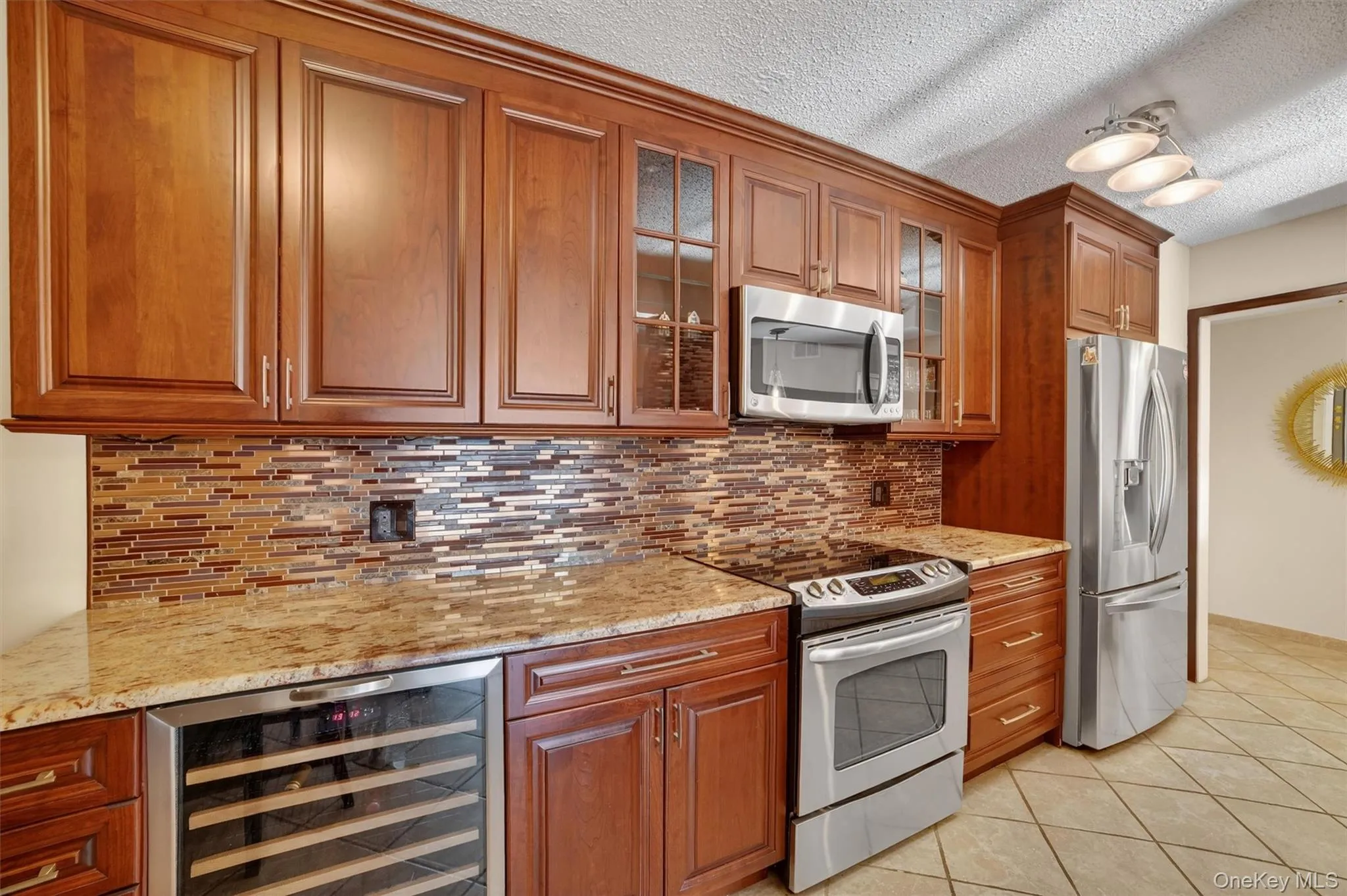 Kitchen with glass insert cabinets, stainless steel appliances, brown cabinetry, beverage cooler, and light tile patterned floors Kitchen with glass insert cabinets, stainless steel appliances, brown cabinetry, beverage cooler, and light tile patterned floors