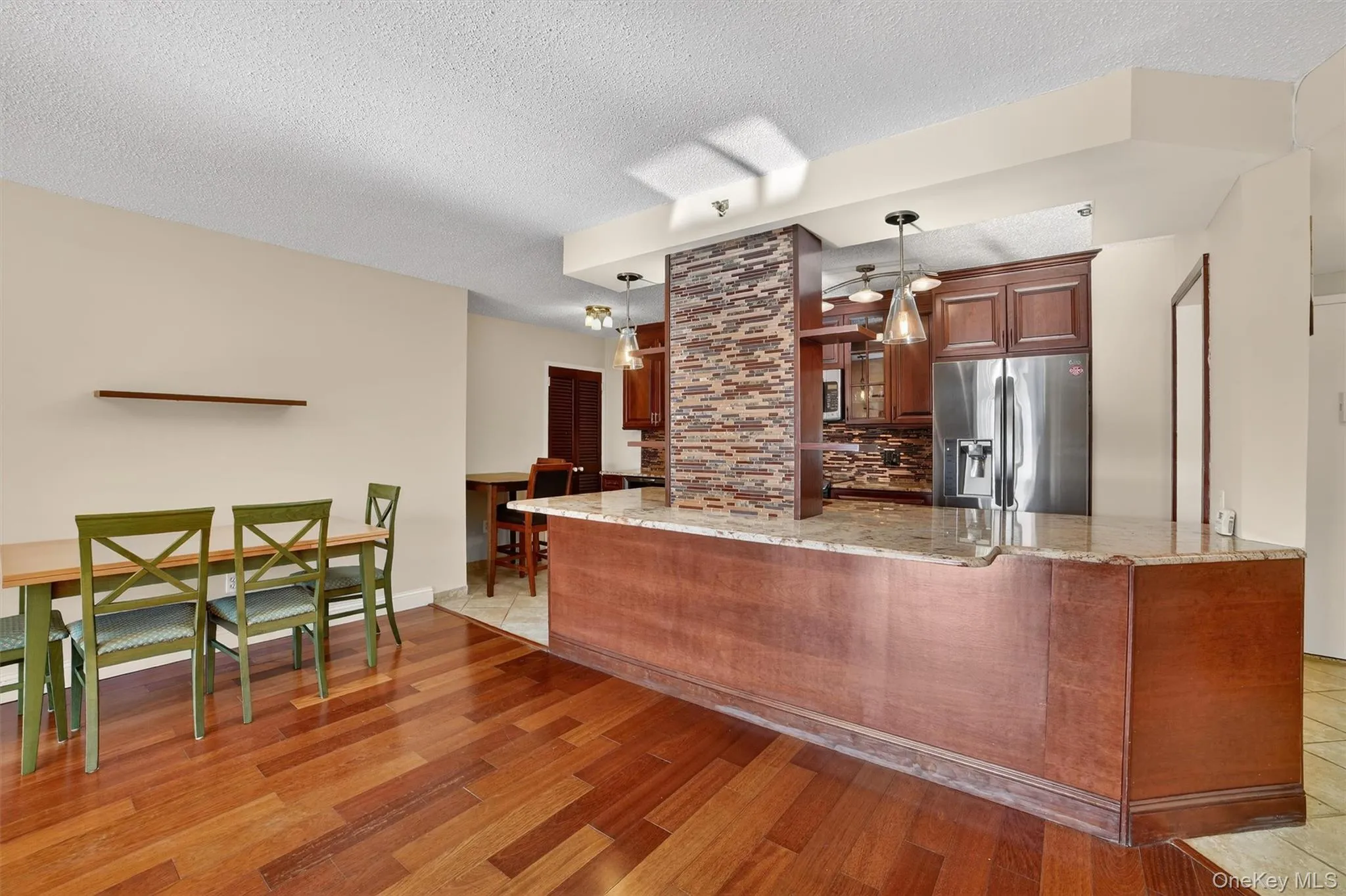 Kitchen featuring appliances with stainless steel finishes, a textured ceiling, light stone counters, pendant lighting, and light wood-style floors Kitchen featuring appliances with stainless steel finishes, a textured ceiling, light stone counters, pendant lighting, and light wood-style floors