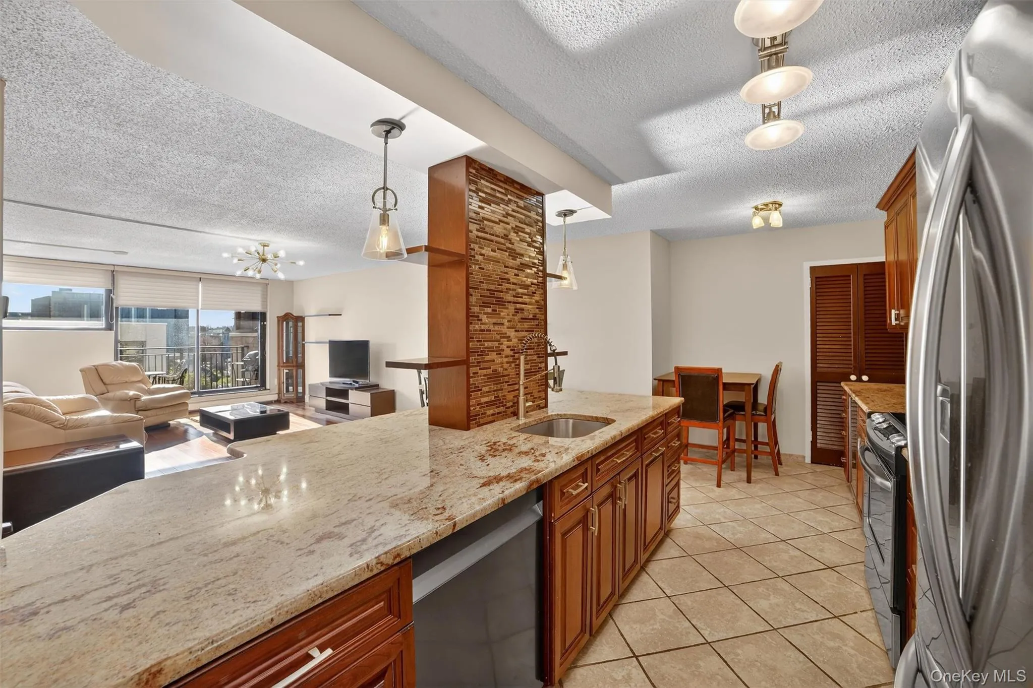 Kitchen featuring a textured ceiling, appliances with stainless steel finishes, light stone countertops, pendant lighting, and open floor plan Kitchen featuring a textured ceiling, appliances with stainless steel finishes, light stone countertops, pendant lighting, and open floor plan
