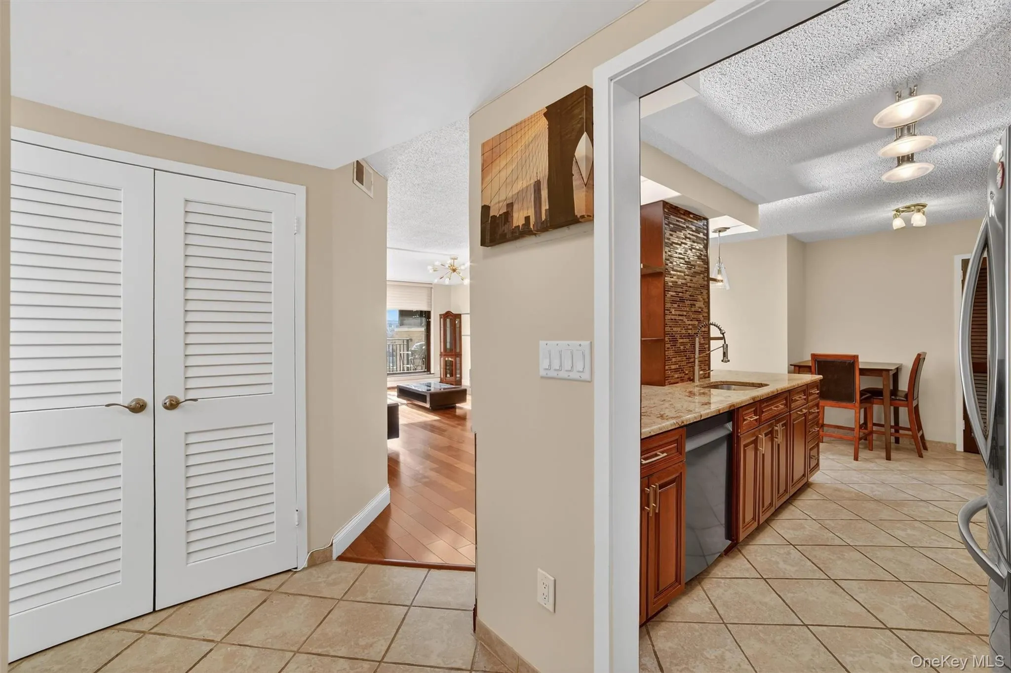 Kitchen featuring a textured ceiling, light tile patterned floors, light stone counters, brown cabinets, and stainless steel appliances Kitchen featuring a textured ceiling, light tile patterned floors, light stone counters, brown cabinets, and stainless steel appliances