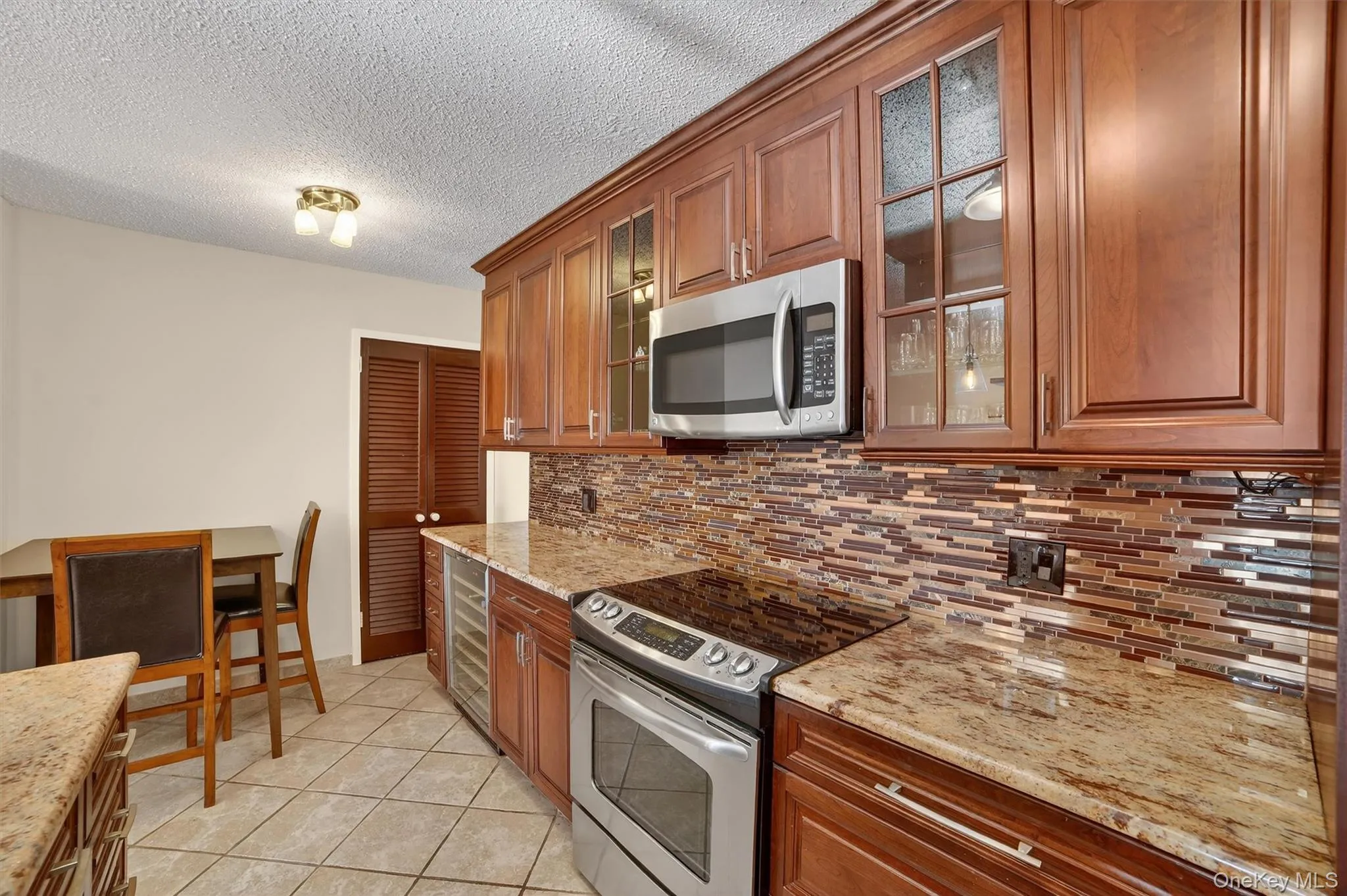 Kitchen with stainless steel appliances, brown cabinetry, wine cooler, a textured ceiling, and light stone countertops Kitchen with stainless steel appliances, brown cabinetry, wine cooler, a textured ceiling, and light stone countertops