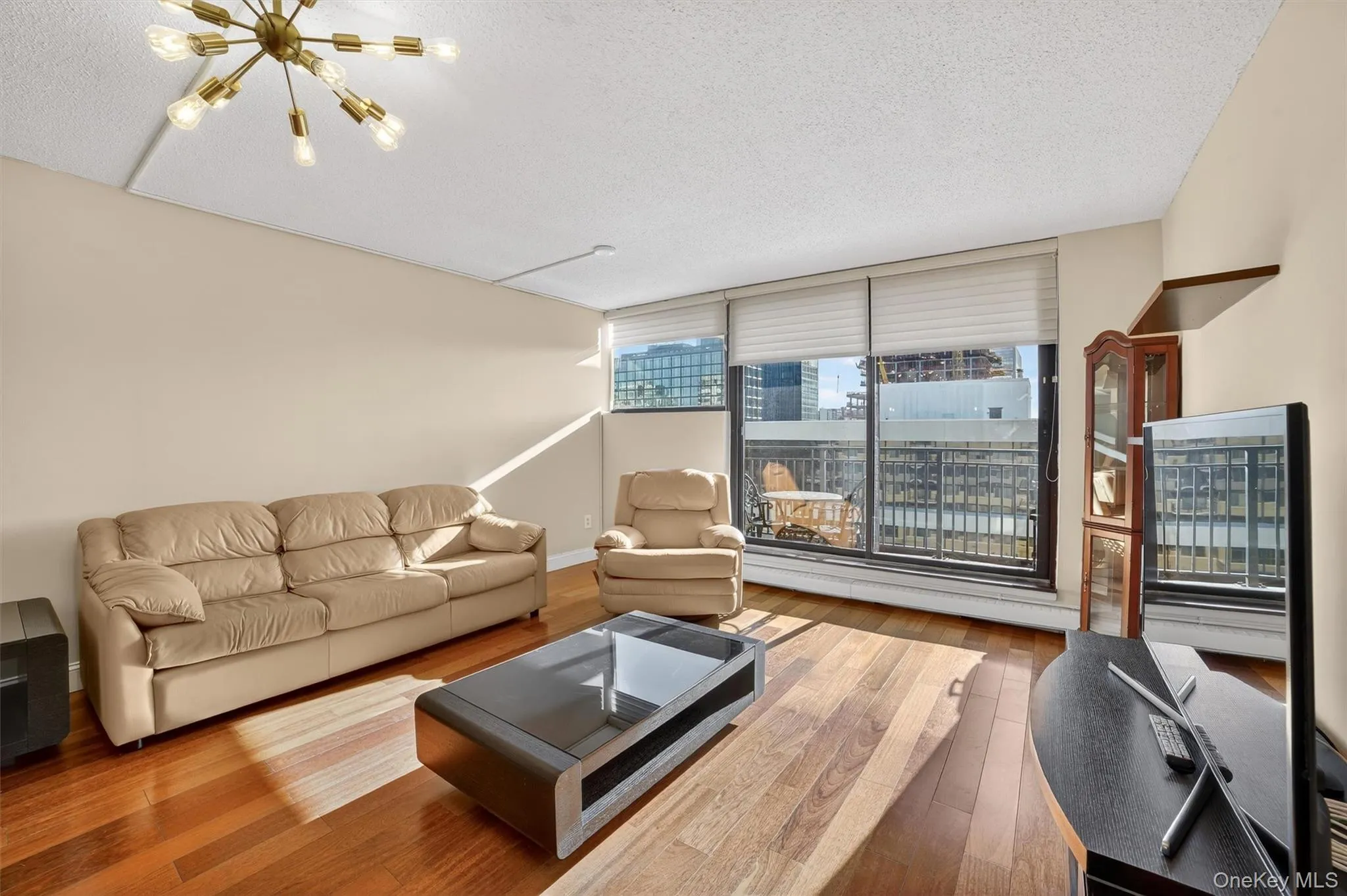 Living room featuring a textured ceiling, wood-type flooring, a chandelier, and a baseboard radiator Living room featuring a textured ceiling, wood-type flooring, a chandelier, and a baseboard radiator