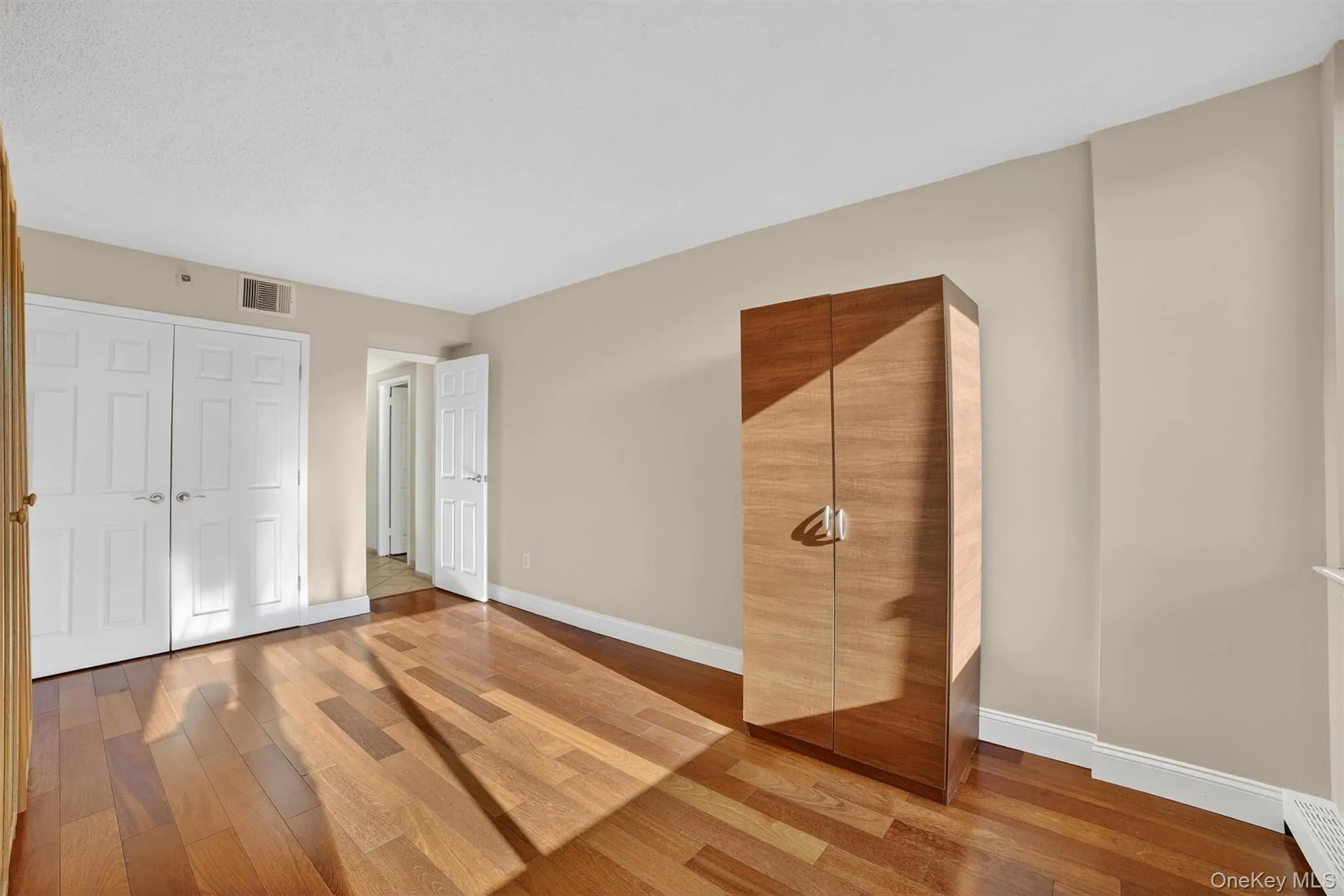 Unfurnished bedroom featuring wood finished floors, a closet, and a baseboard radiator Unfurnished bedroom featuring wood finished floors, a closet, and a baseboard radiator