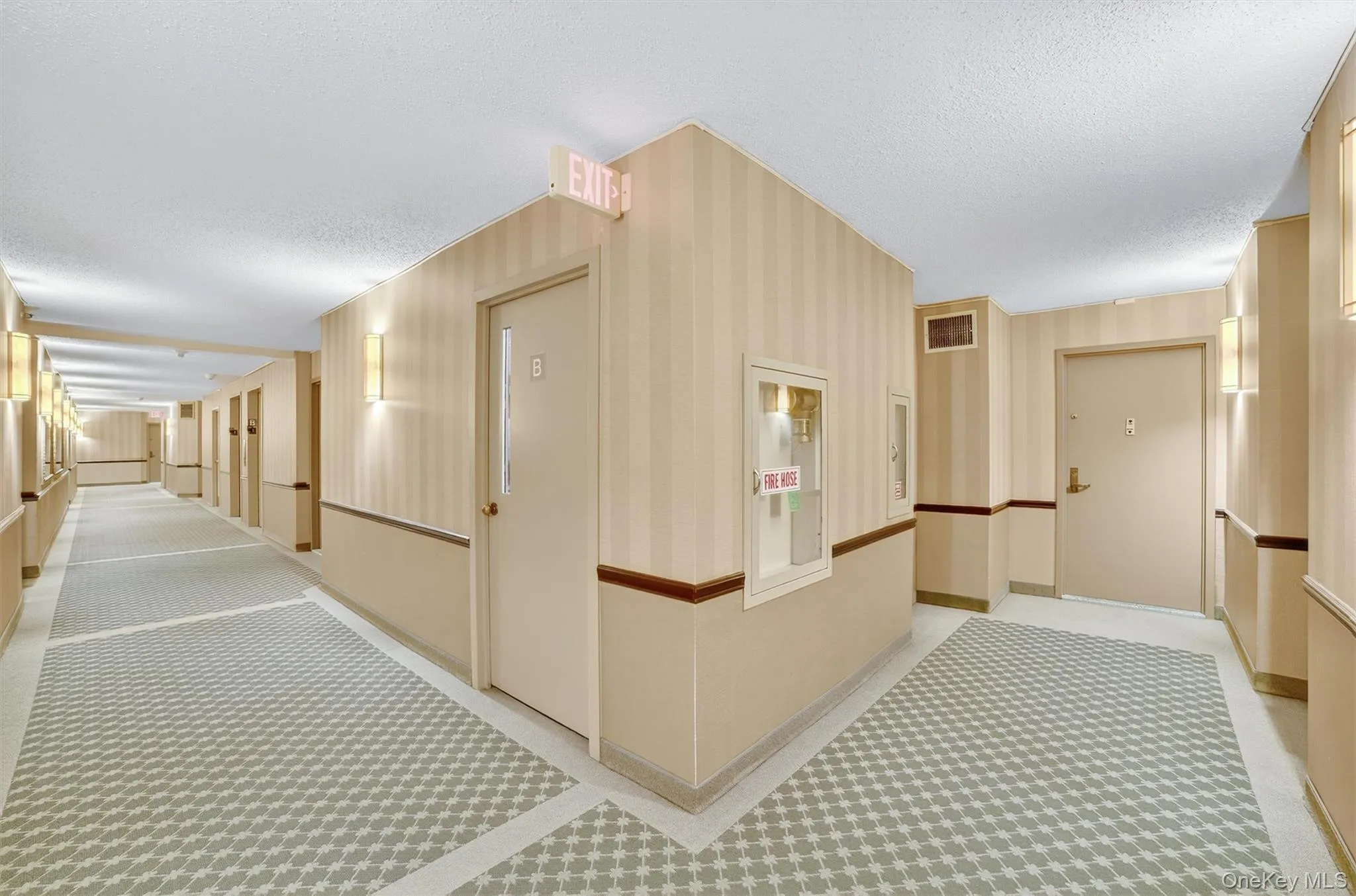 Hall featuring a textured ceiling and light carpet Hall featuring a textured ceiling and light carpet