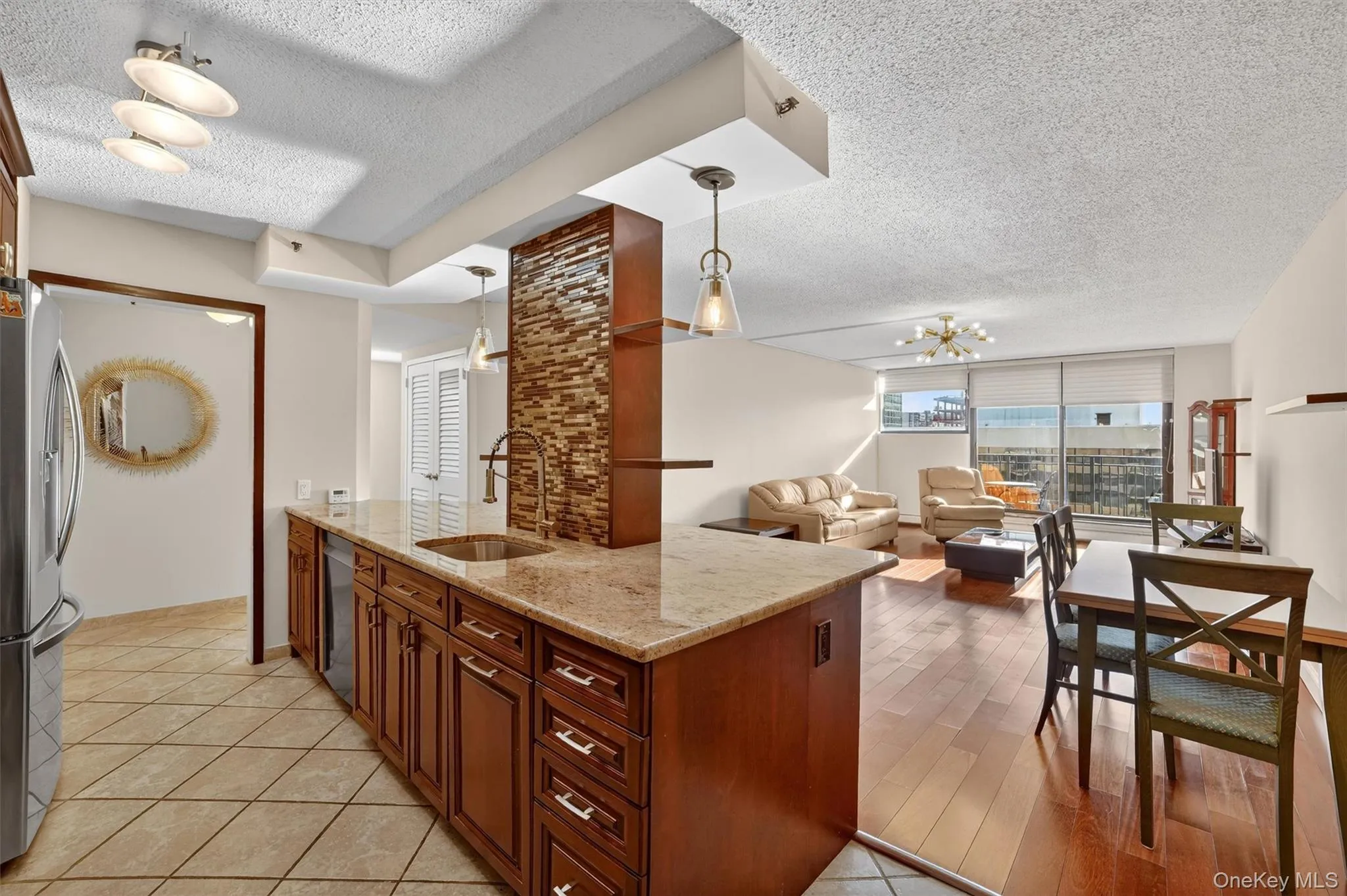 Kitchen featuring a textured ceiling, light stone countertops, hanging light fixtures, stainless steel appliances, and open floor plan Kitchen featuring a textured ceiling, light stone countertops, hanging light fixtures, stainless steel appliances, and open floor plan