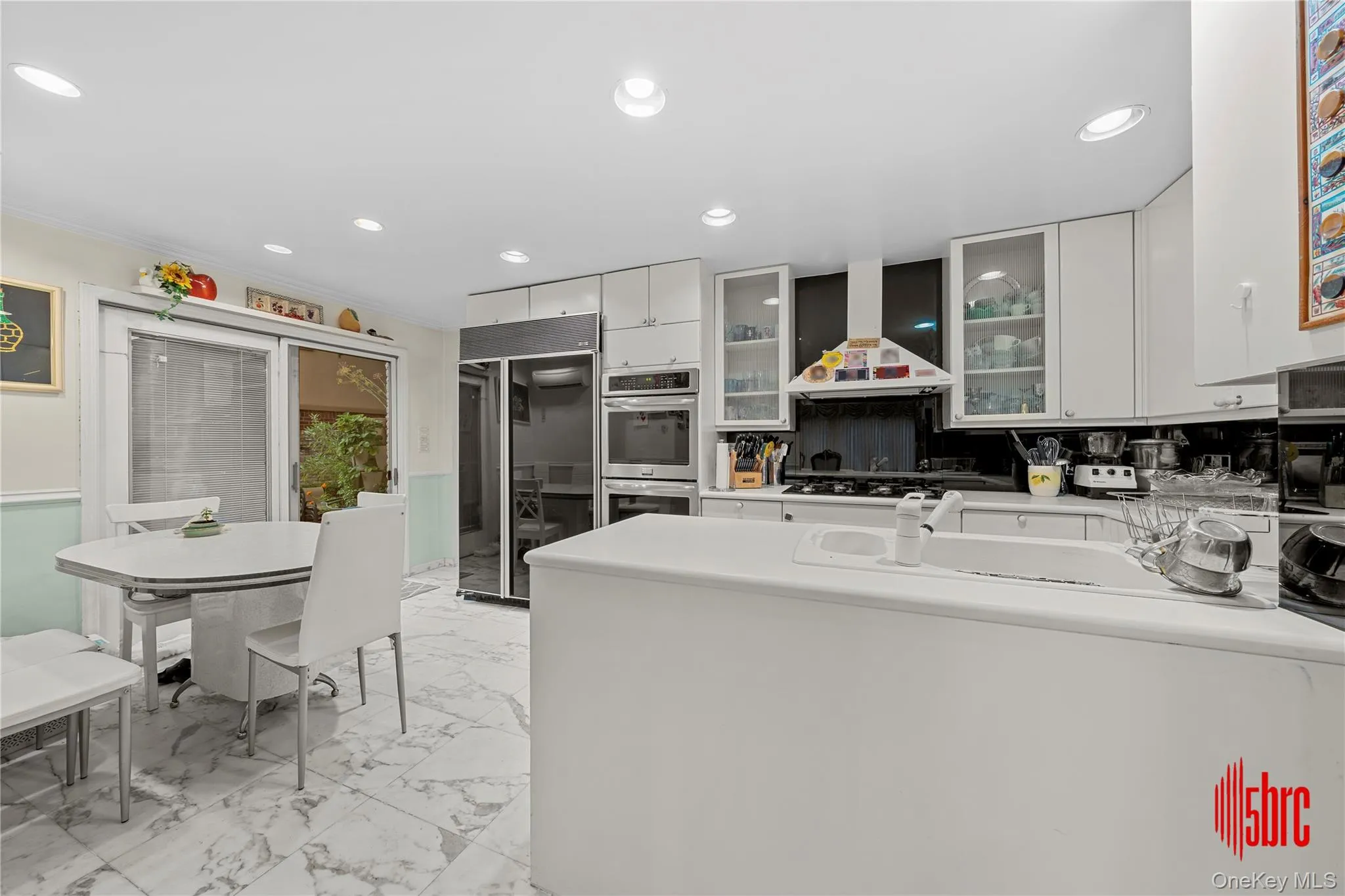 Kitchen with recessed lighting, fridge, light marble finish floors, light countertops, and glass insert cabinets Kitchen with recessed lighting, fridge, light marble finish floors, light countertops, and glass insert cabinets