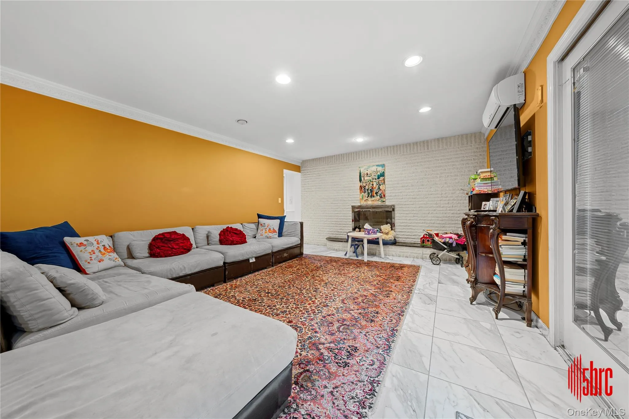 Living room featuring ornamental molding, recessed lighting, light marble finish floors, an AC wall unit, and a fireplace Living room featuring ornamental molding, recessed lighting, light marble finish floors, an AC wall unit, and a fireplace